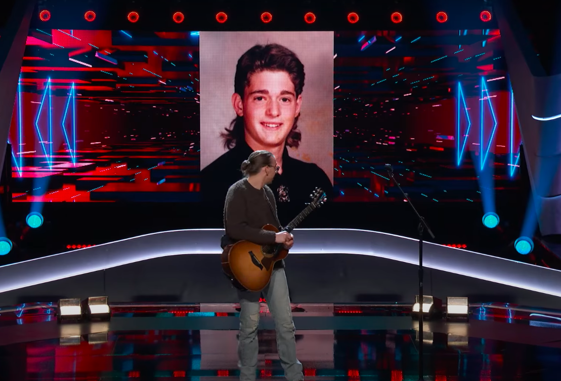 Ethan Eckenroad looking back at a throwback photo of Michael Bublé with a mullet. | Source: YouTube/The Voice