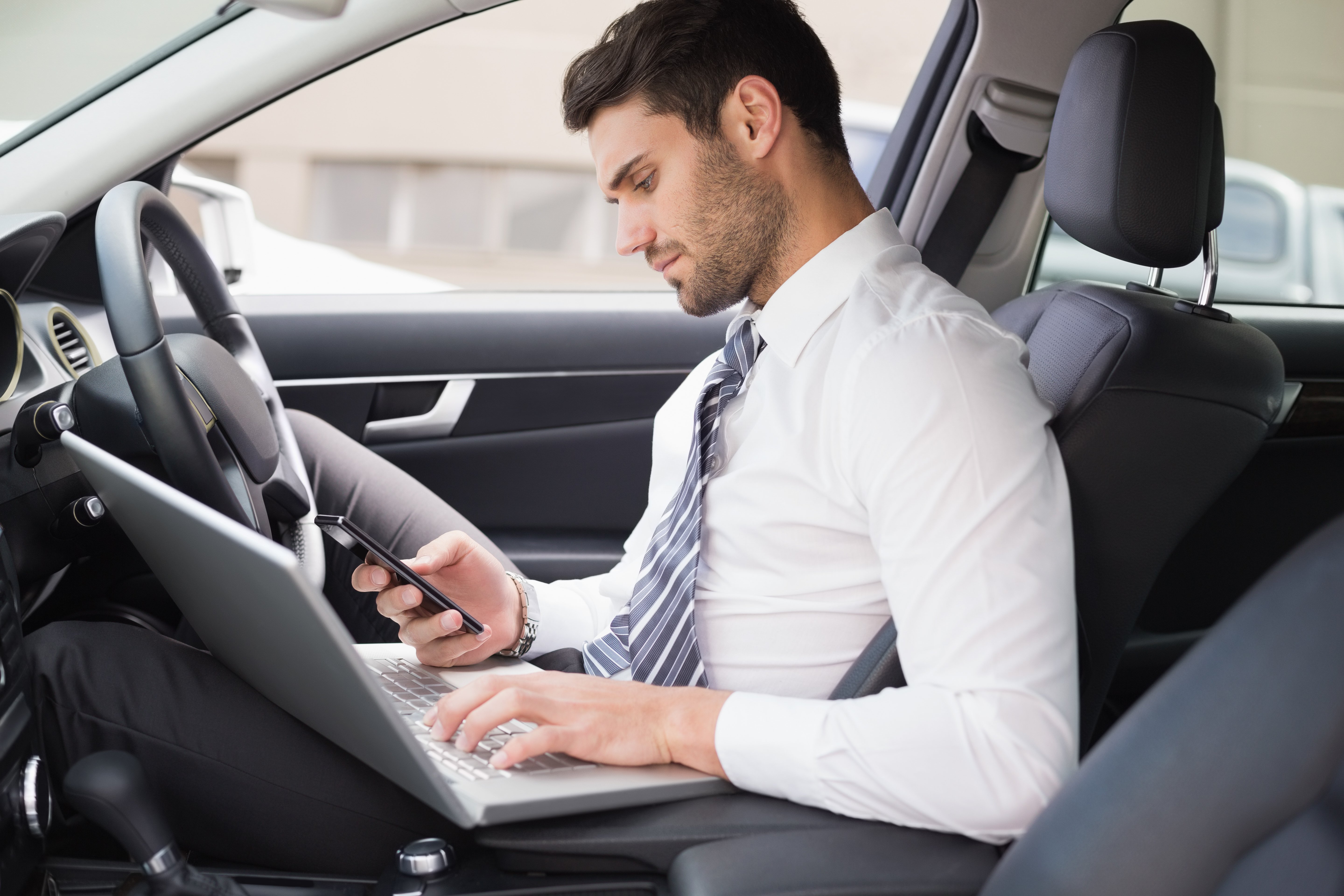 Hombre con computadora portátil en auto. | Foto: Shutterstock