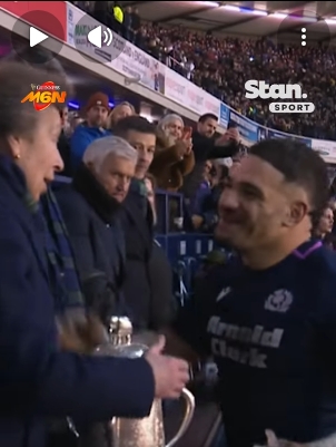 With the trophy poised between them, Sione Tuipulotu steps closer to the Princess Royal, his expression a mix of pride and adrenaline after Scotland's hard-fought 31–20 victory. The princess appears attentive and composed, mid-conversation, as the stadium backdrop hums with applause and raised phones recording the moment. | Source: YouTube/StanSportAU