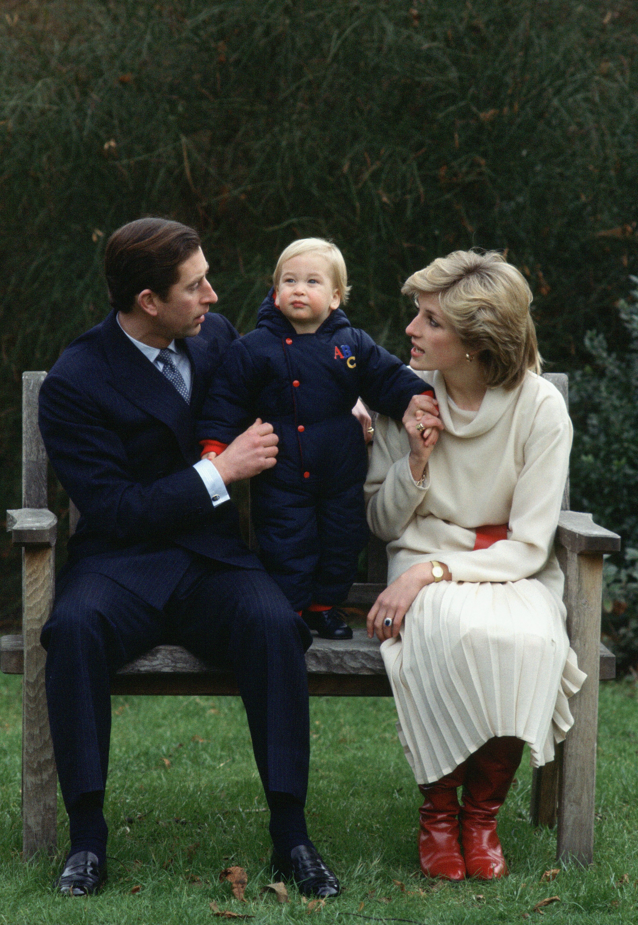 King Charles III and Princess Diana sitting on a bench for a photocall with their son, Prince William (age approximately 18 months), in their garden at Kensington Palace. | Source: Getty Images