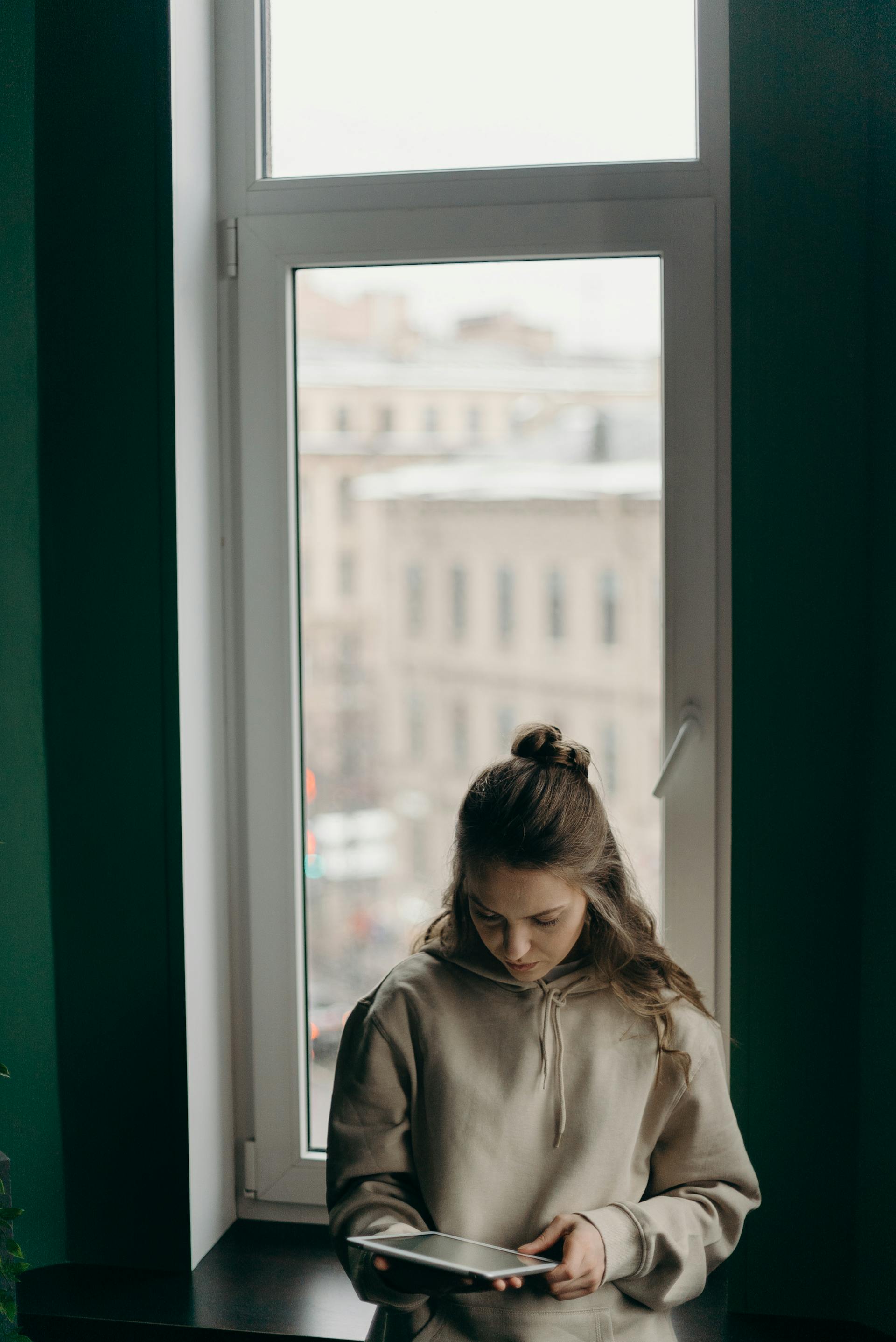 A woman looking at her iPad while standing near the window | Source: Pexels