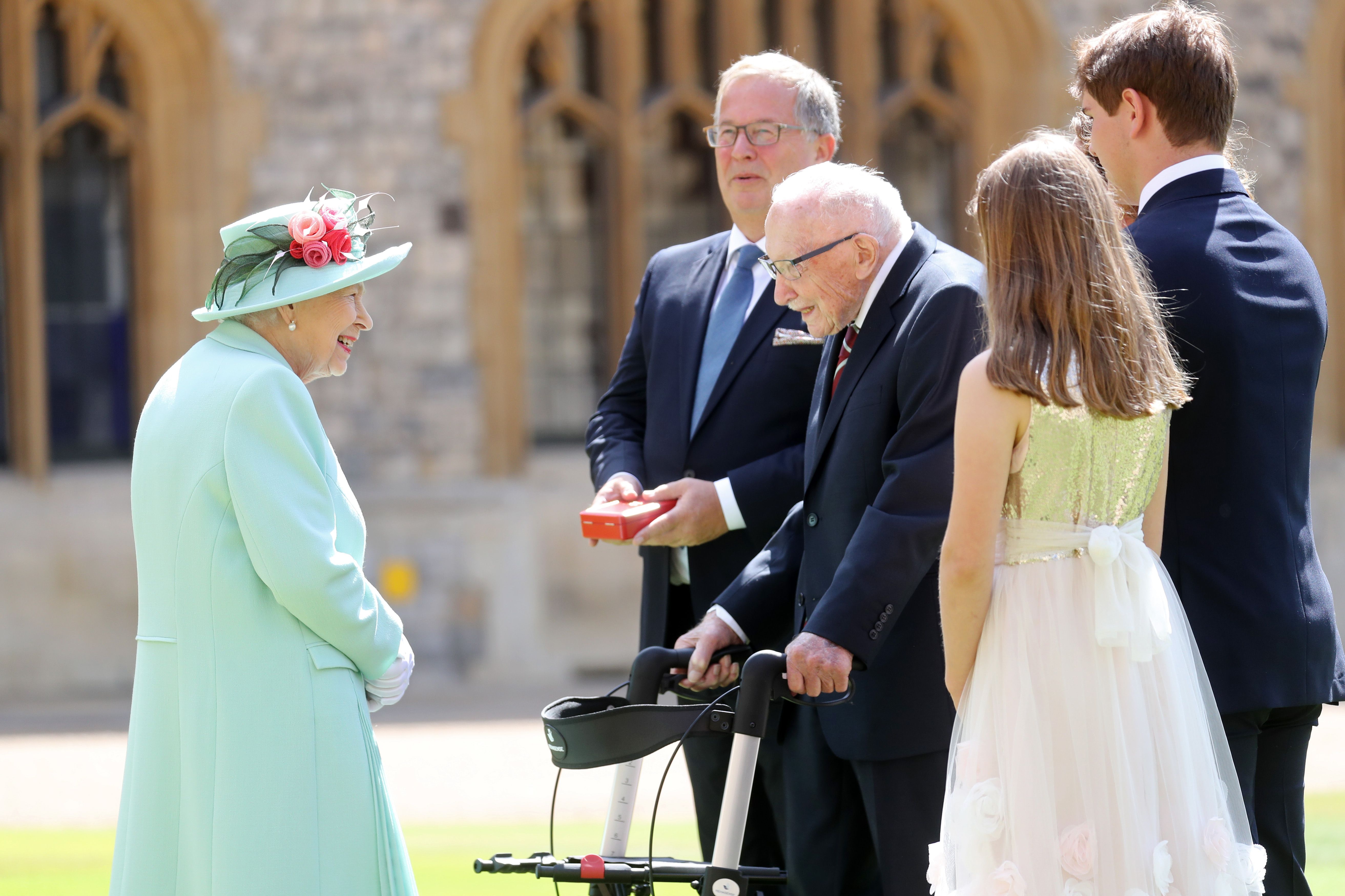 Queen Elizabeth II talks Captain Sir Thomas Moore and his family after awarding him with the insignia of Knight Bachelor at Windsor Castle on July 17, 2020 in Windsor, England. | Photo: Getty Images