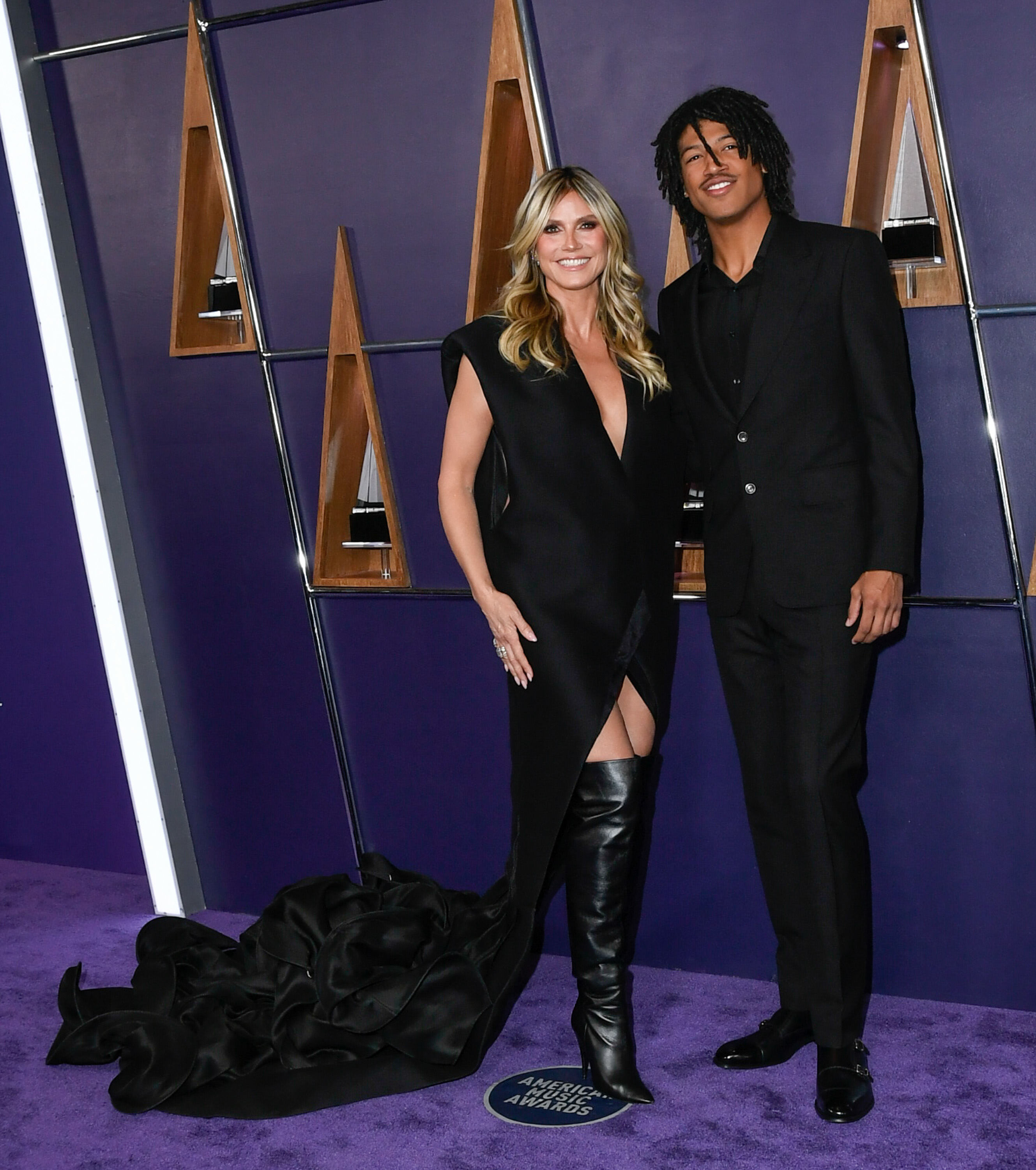 With his shoulders squared and a slight smile, Henry Samuel stands confidently beside Heidi Klum as they pose in sync for photographers on the 2025 AMAs carpet.