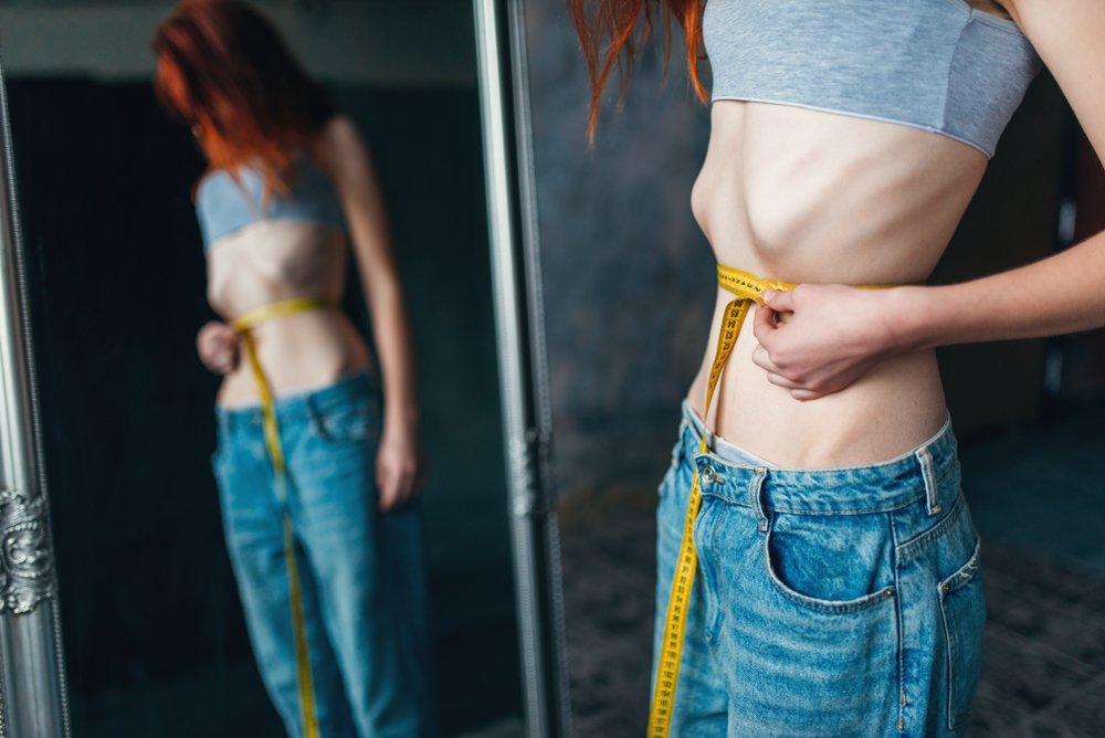 Mujer mide su cintura y se mira en el espejo. Fuente: Shutterstock