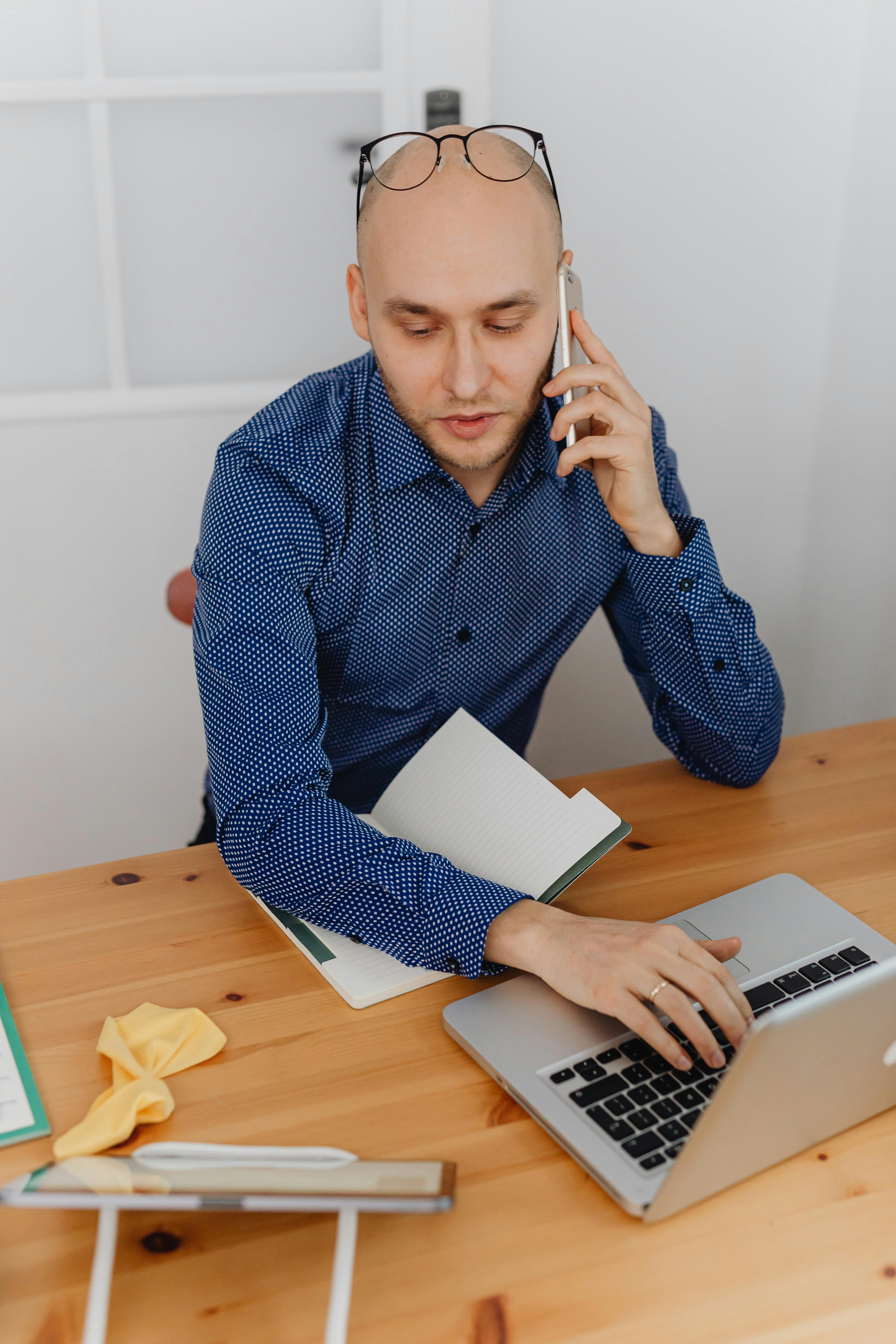 A formally dressed man on a phone call while working on a laptop | Source: Pexels