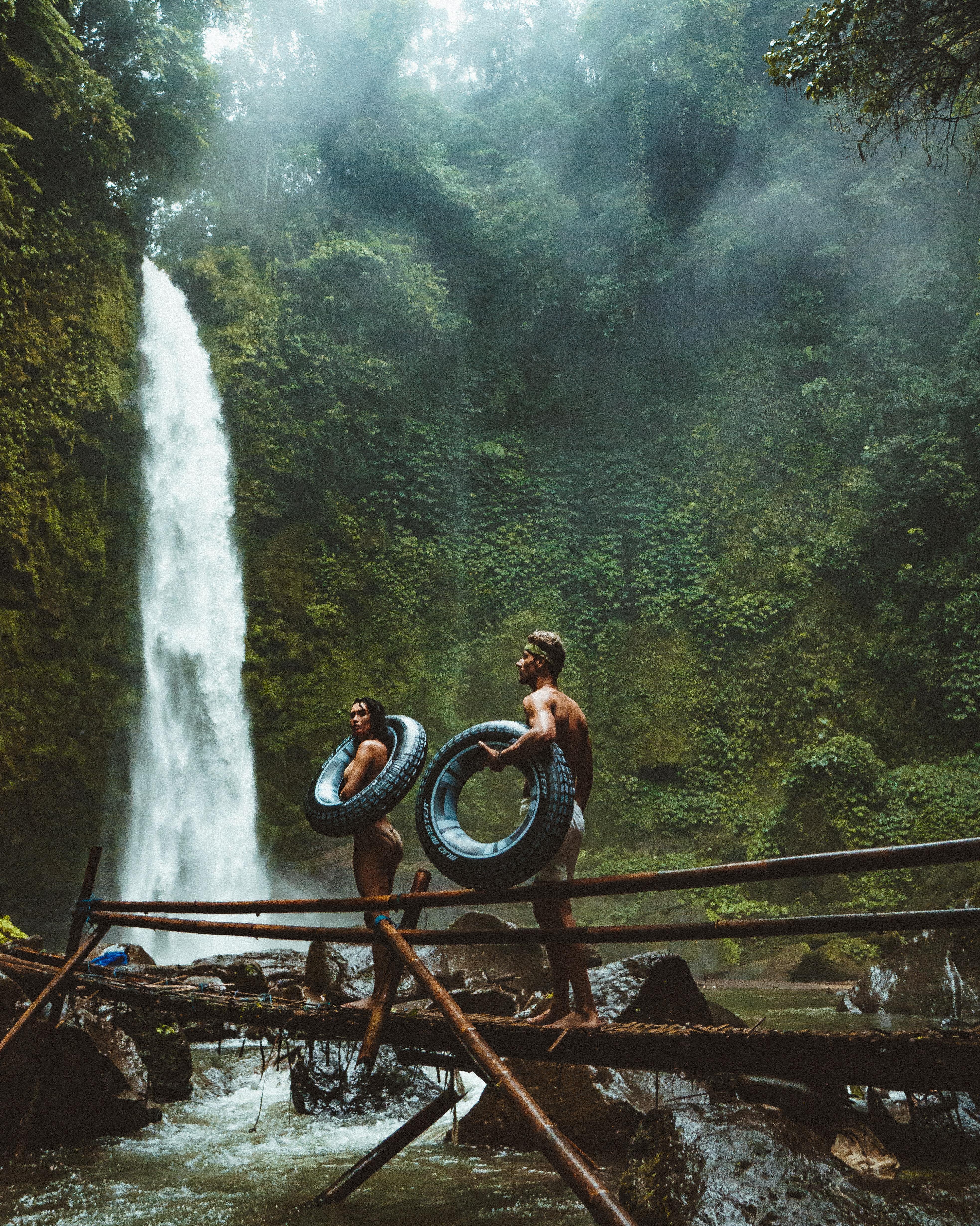 A couple holding float tubes while standing by a waterfall. | Source: Pexels