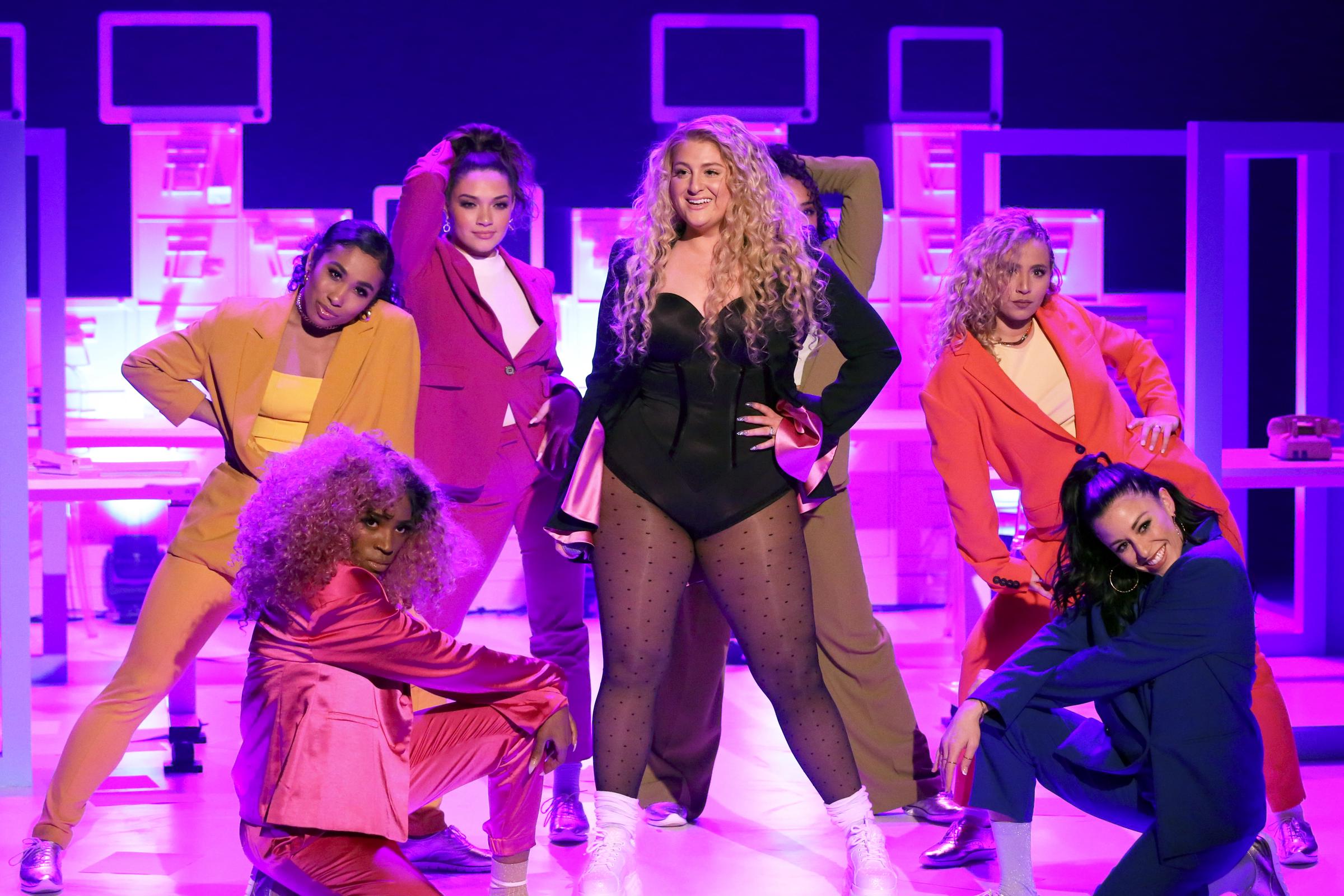Meghan Trainor performs on "The Tonight Show" with a crew of backup dancers, commanding attention in a black leotard and polka dot tights against a glowing pink-lit set.