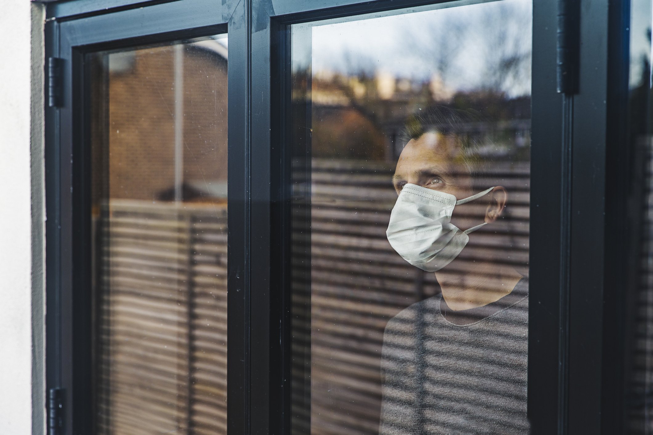 Mann mit Maske schaut aus dem Fenster | Quelle: Getty Images