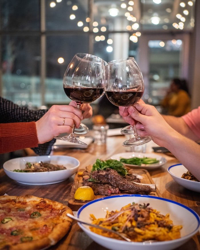 Four hands holding glasses of wine and food on the table | Source: Unsplash