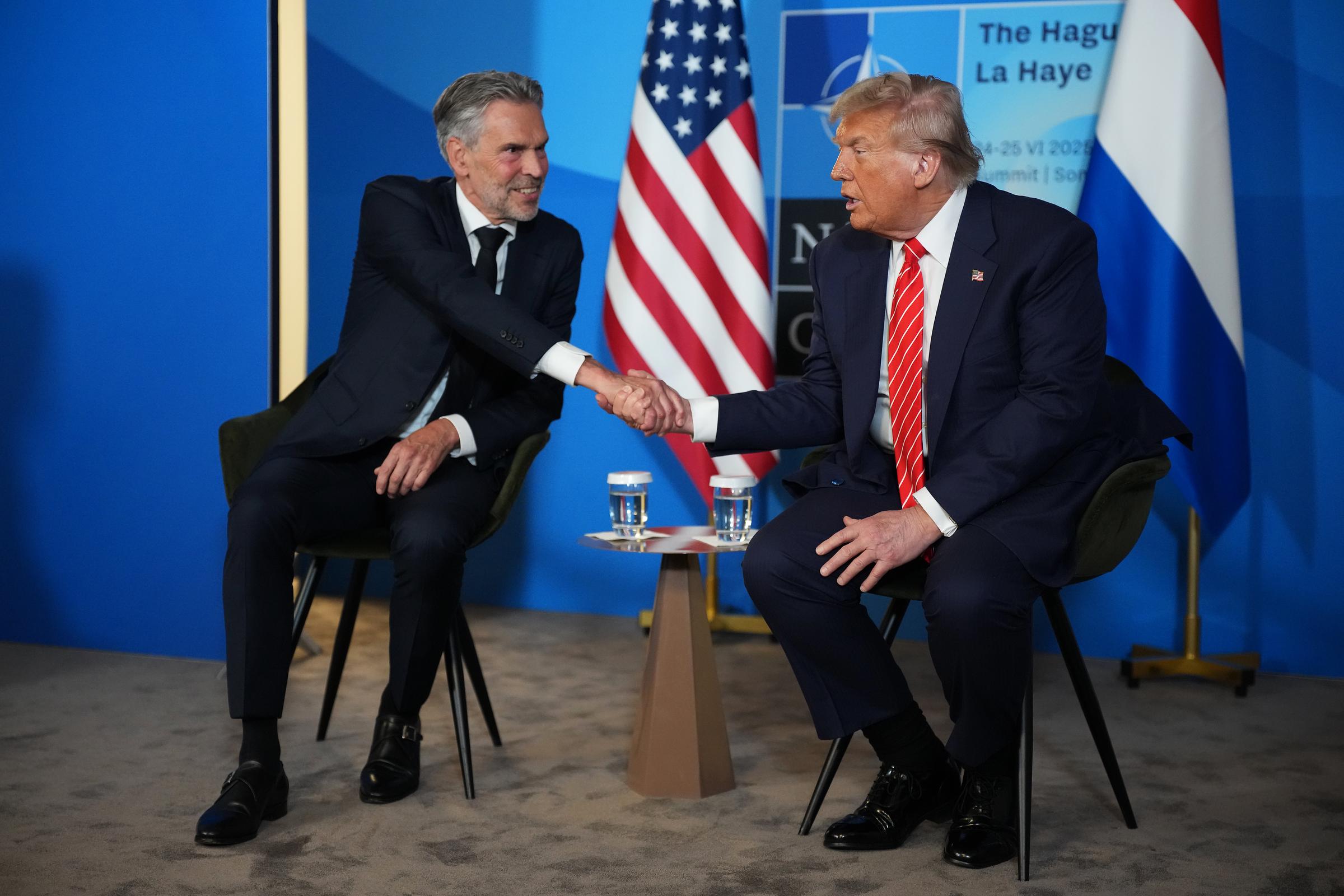 Dutch Prime Minister Dick Schoof and Trump meet on the second day of the 2025 NATO Summit, beginning with a formal handshake before easing into conversation. Seated next to each other, glasses of water placed neatly beside them, the two leaders appear focused as they dive into discussions.