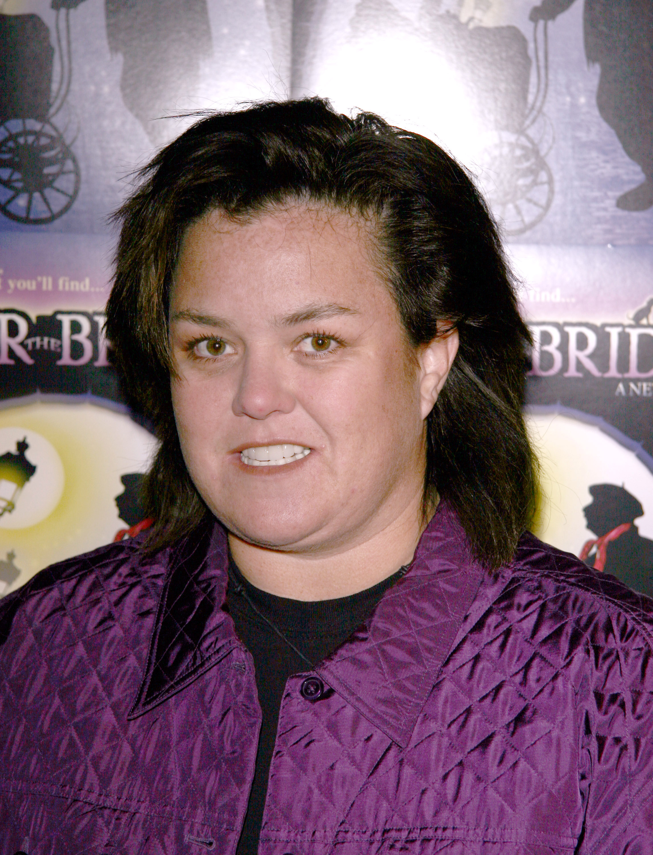 Rosie O'Donnell attends the opening night of "Under the Bridge" at The Zipper Theater in New York City, posing in front of promotional posters in a shiny purple jacket.