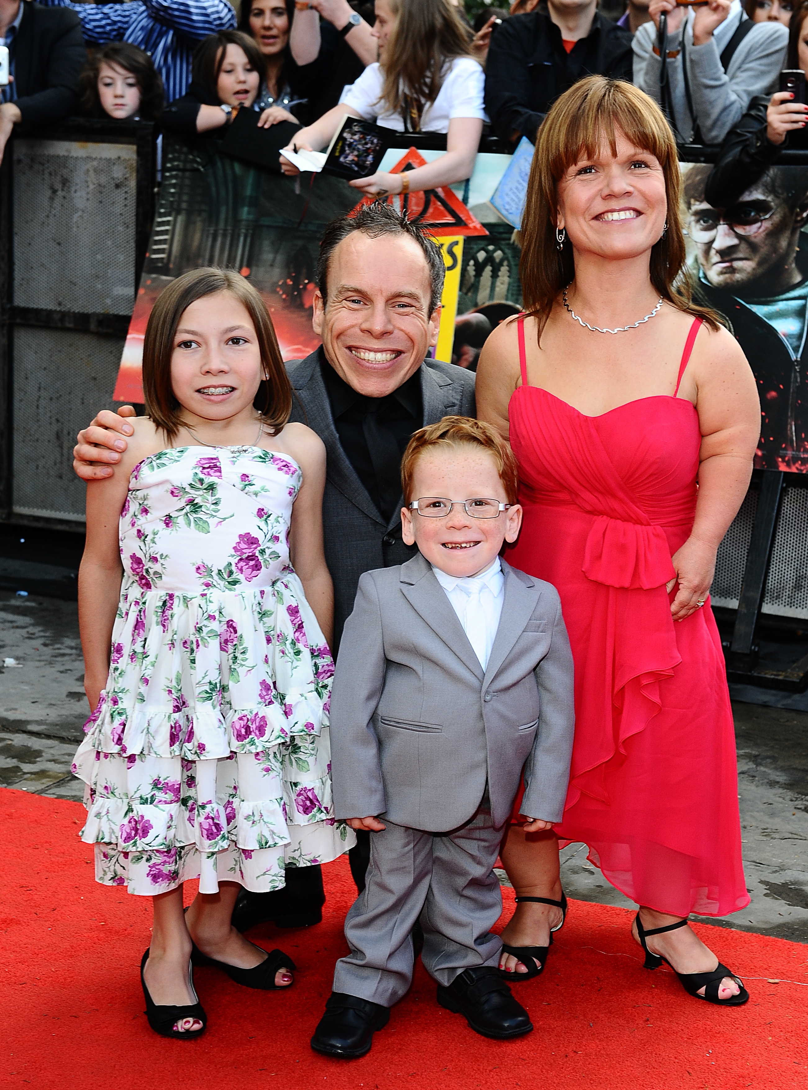 A younger Warwick Davis beams on the red carpet at the world premiere of "Harry Potter and the Deathly Hallows: Part 2" on 7 July 2011, his arm around a then-young Annabelle while his late wife Samantha smiles warmly beside them, Harrison front and centre in a dapper grey suit. It is a snapshot of a family at the peak of a glittering career — and a poignant reminder of what the actor carried with him to Windsor Castle on Wednesday.