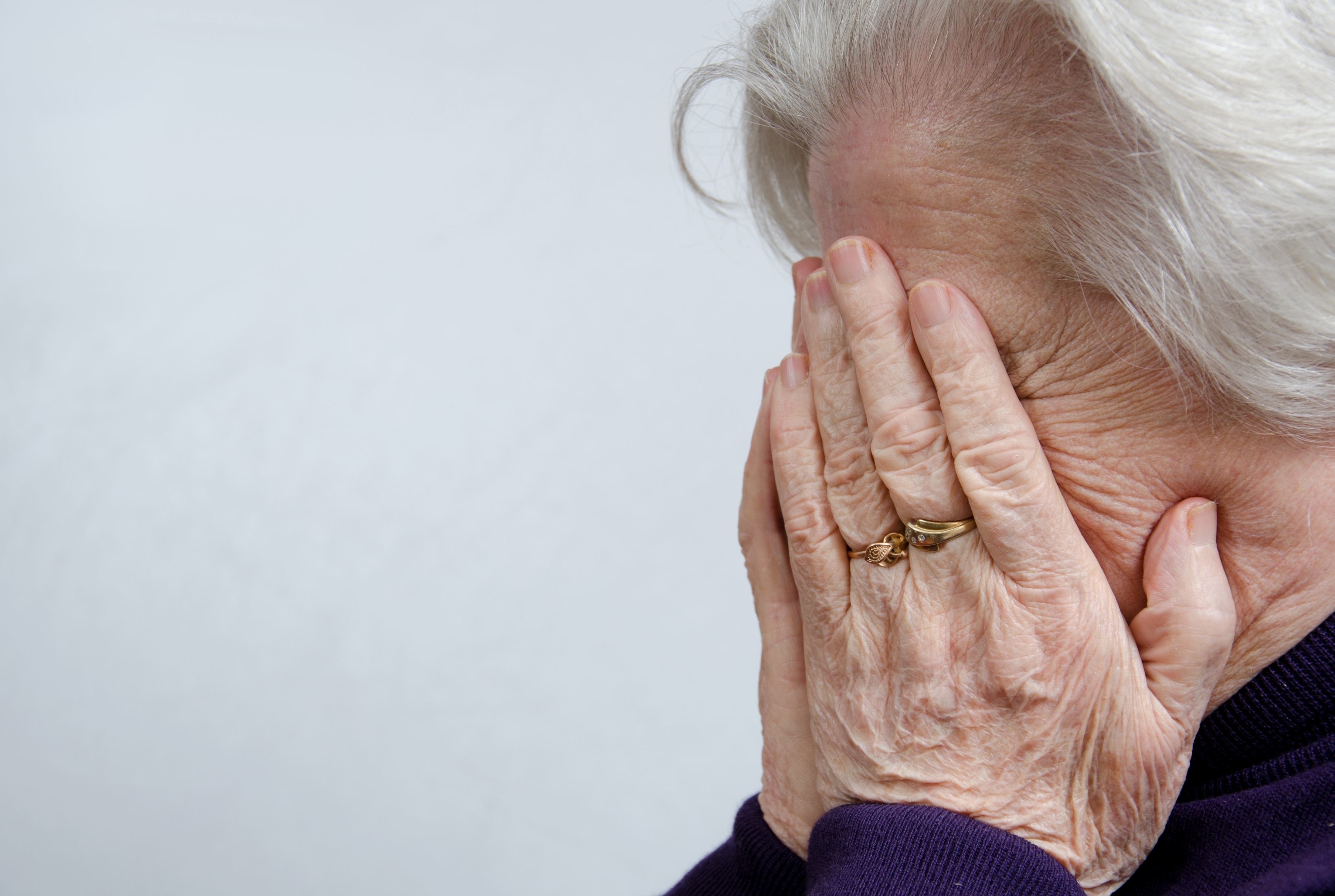 Eine weißhaarige Frau, die ihr Gesicht mit ihren Händen bedeckt | Quelle: Shutterstock