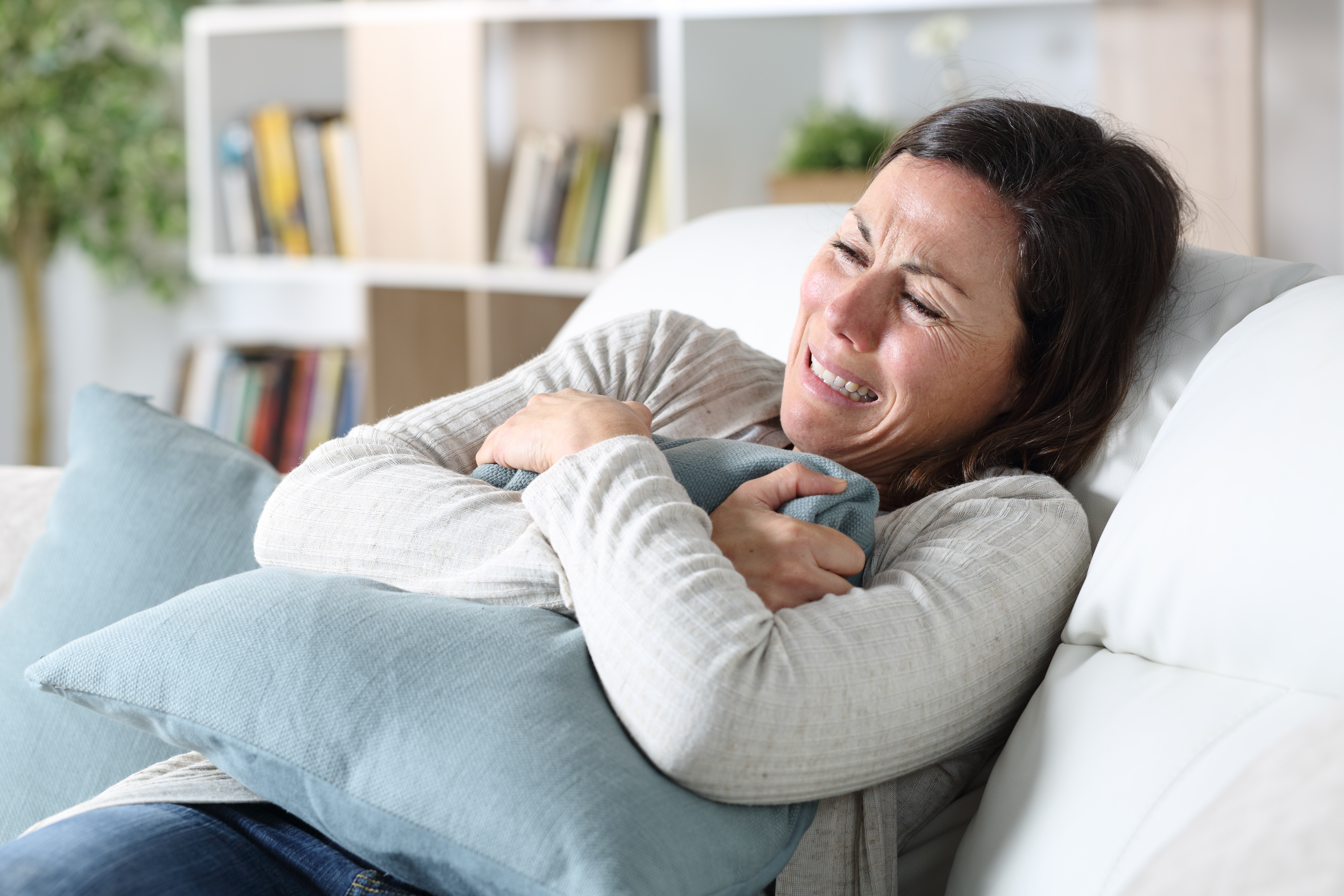 Sad adult woman crying sitting on the sofa holding pillow in the living room at home | Source: Shutterstock.com
