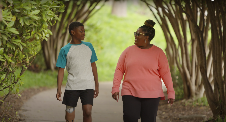 A screenshot from a YouTube video of Parker and his mother taking a walk in a park, posted on July 6, 2022 | Source: YouTube.com/Shriners Children's