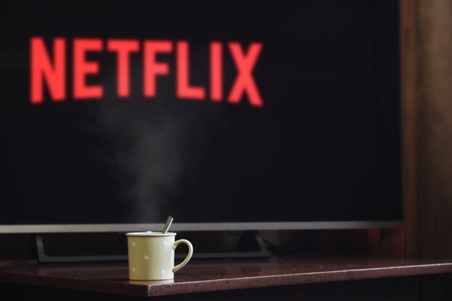 Cup near flat screen television turned onto Netflix | Photo: Pexels