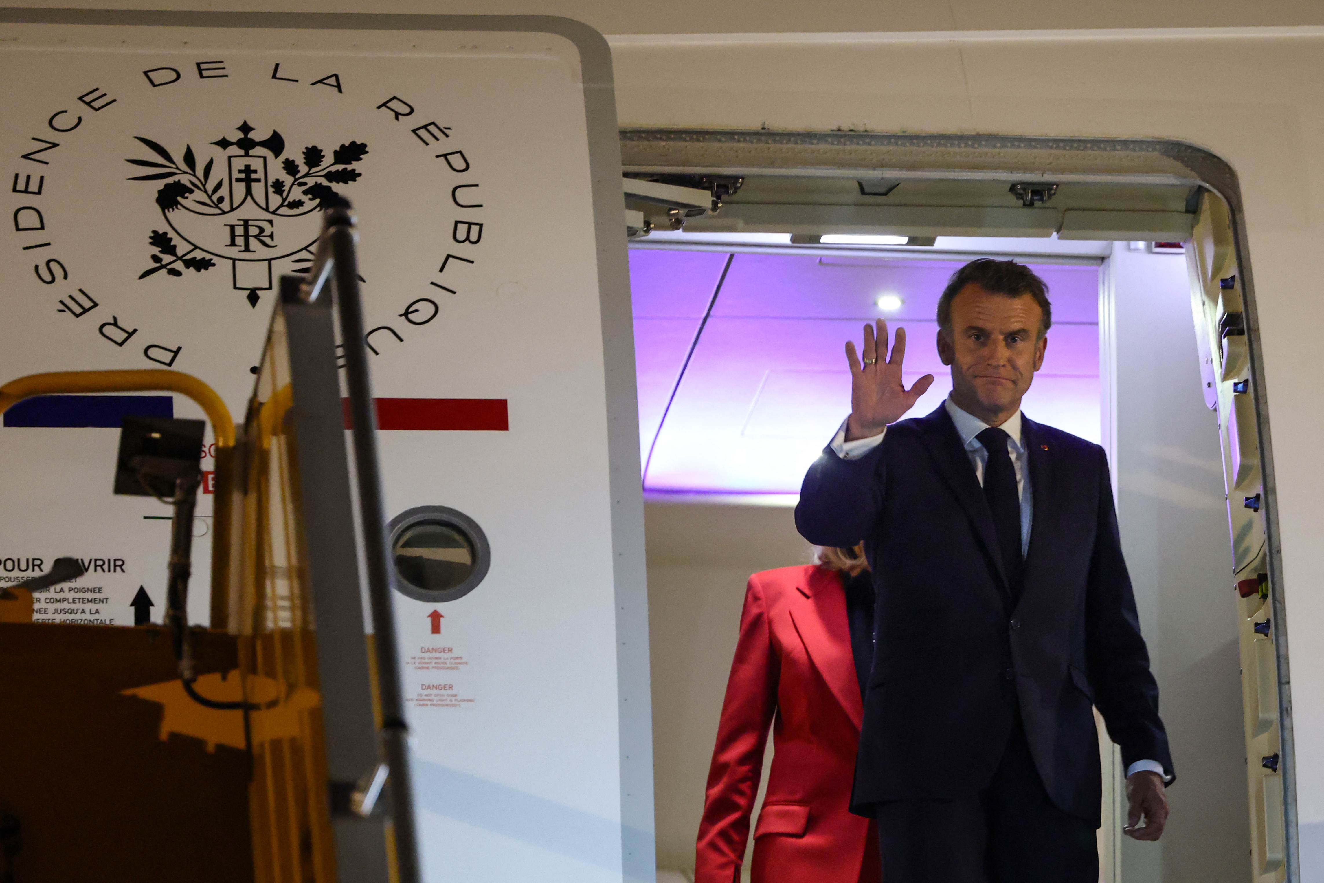 Emmanuel Macron waving as Brigitte Macron walks behind him. | Source: Getty Images