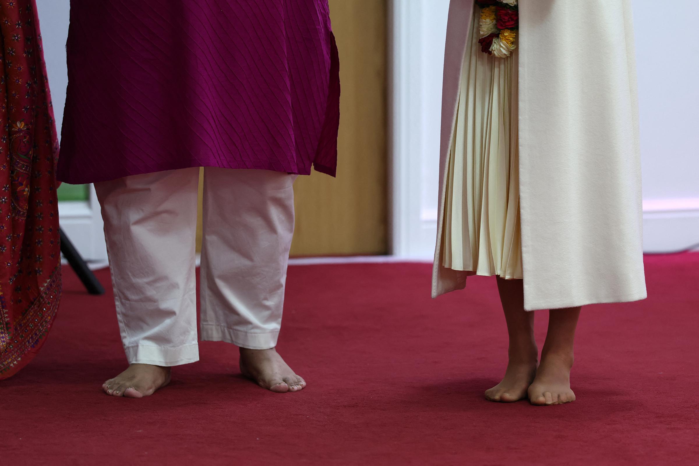 Catherine, Princess of Wales, stands barefoot on the red carpet inside the Shreeji Dham Haveli Hindu Temple in Leicester on March 5, 2026. Removing her shoes in keeping with temple tradition, the Princess of Wales takes part in the visit with quiet respect, her cream pleated skirt visible beside a fellow attendee during the religious ceremony.