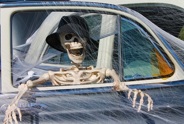 Skeleton sits open-mouthed in a web-covered car wearing a black hat | Photo: Pixabay