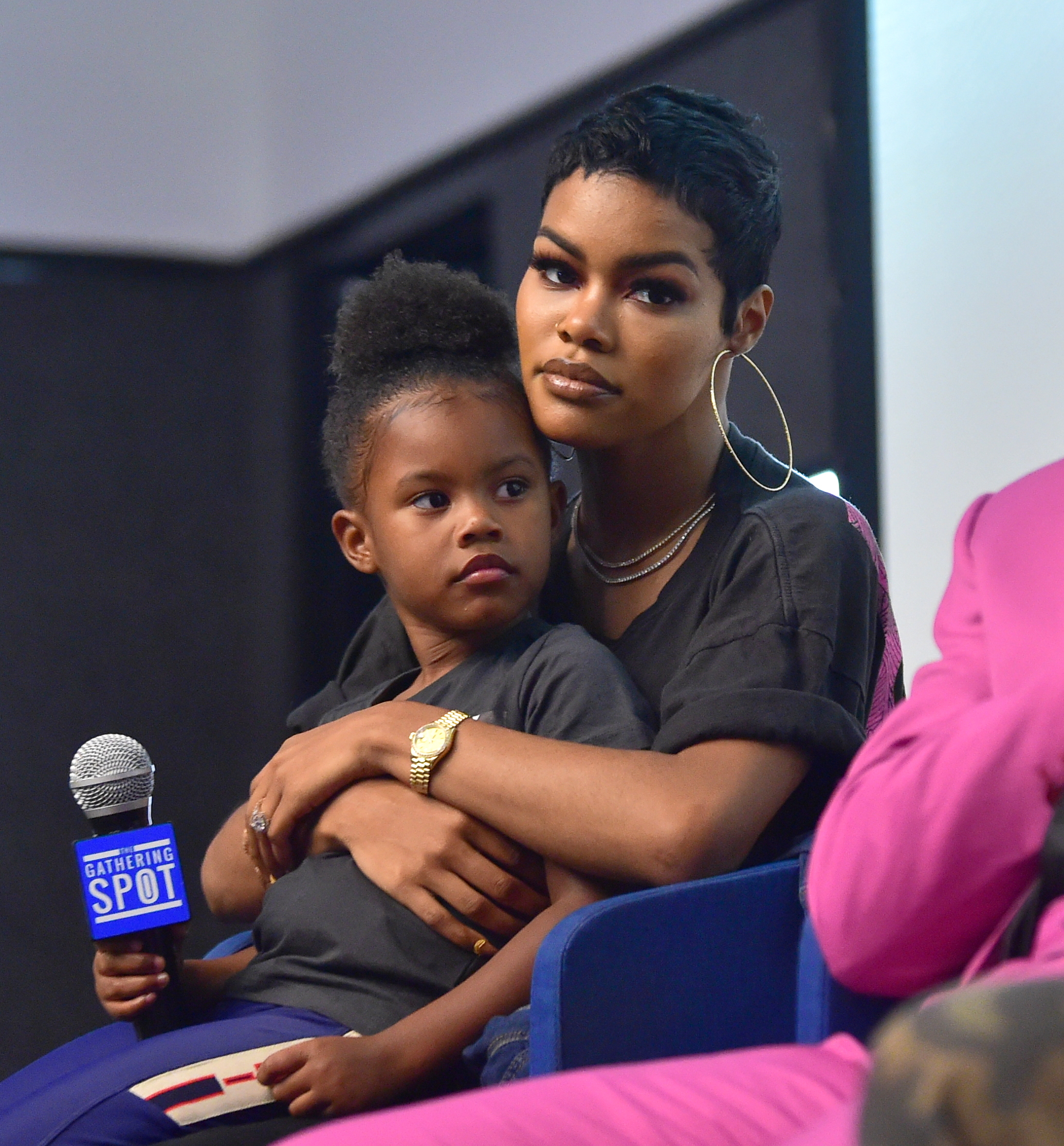Teyana Taylor holds Iman Tayla "Junie" Shumpert Jr. during a screening at The Gathering Spot in Atlanta. Junie grips a microphone as Teyana watches calmly from their panel seats.