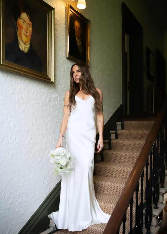 Mel C shared a series of official wedding portraits after the ceremony, offering a closer look at the sleek satin gown that sparked so much discussion online. The staircase setting highlighted the dress's clean silhouette and understated design. | Source: Instagram/timmsy