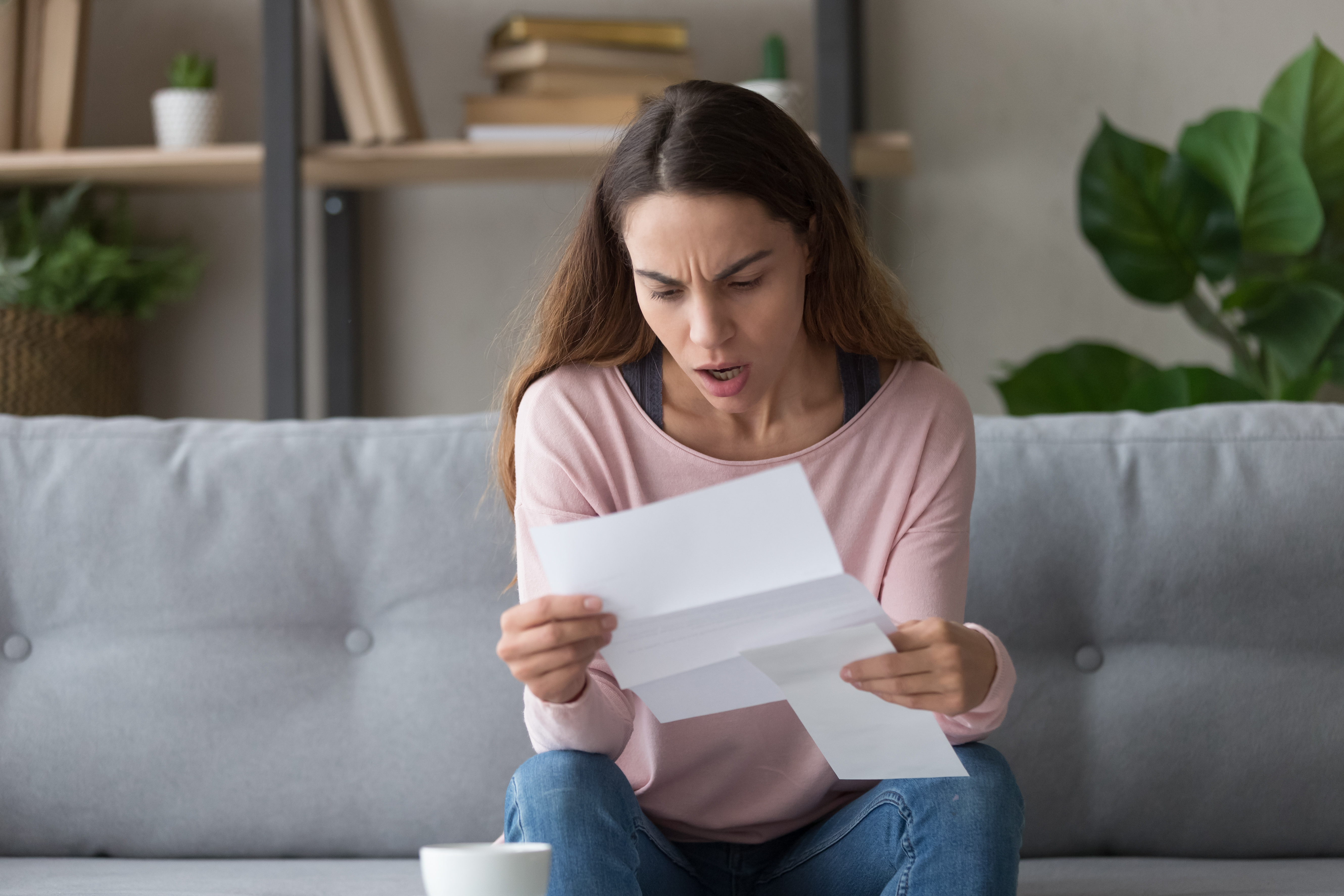 A shocked woman reading a letter while seated | Source: Shutterstock