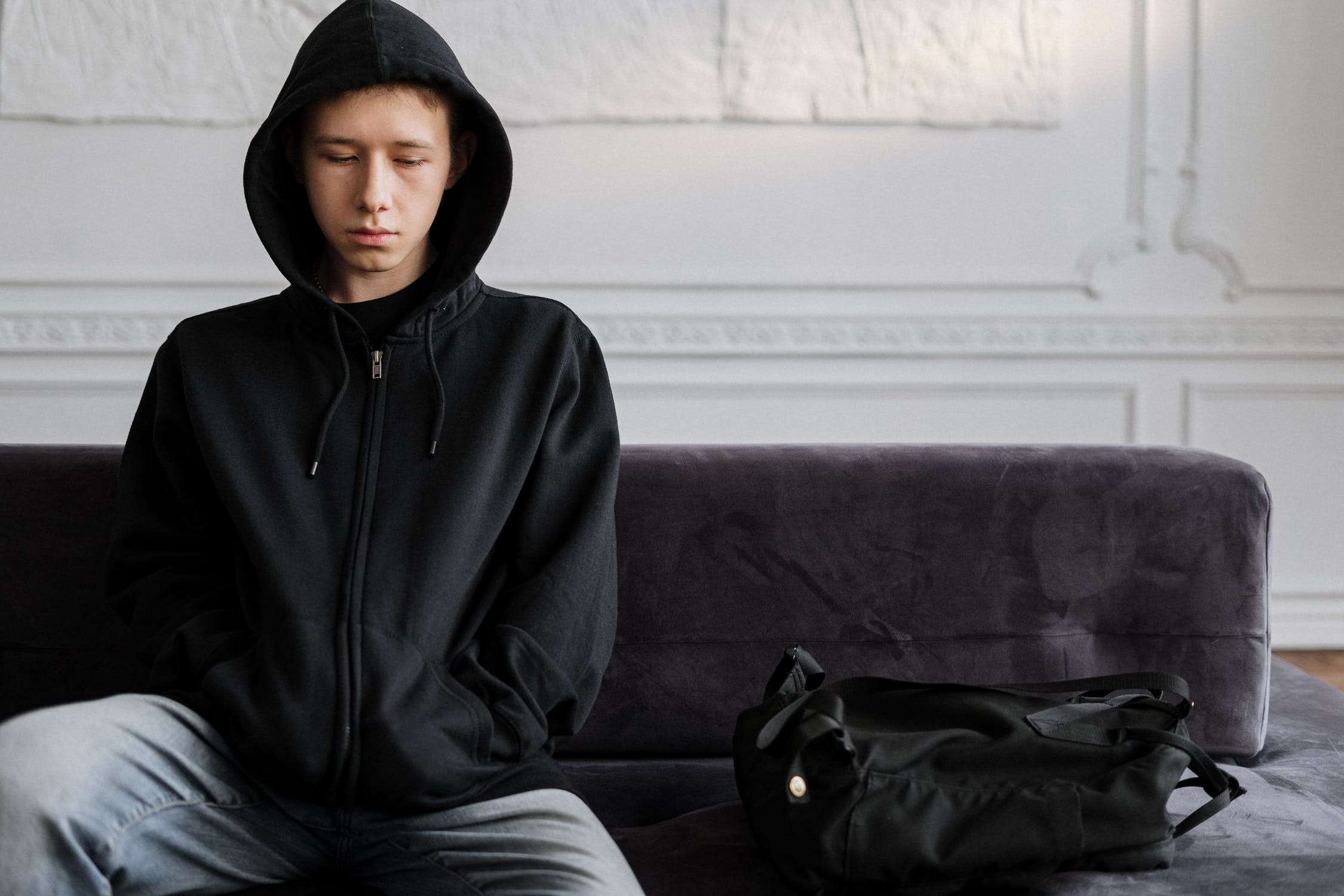 Sad-looking teenager sitting next to a purse | Source: Pexels