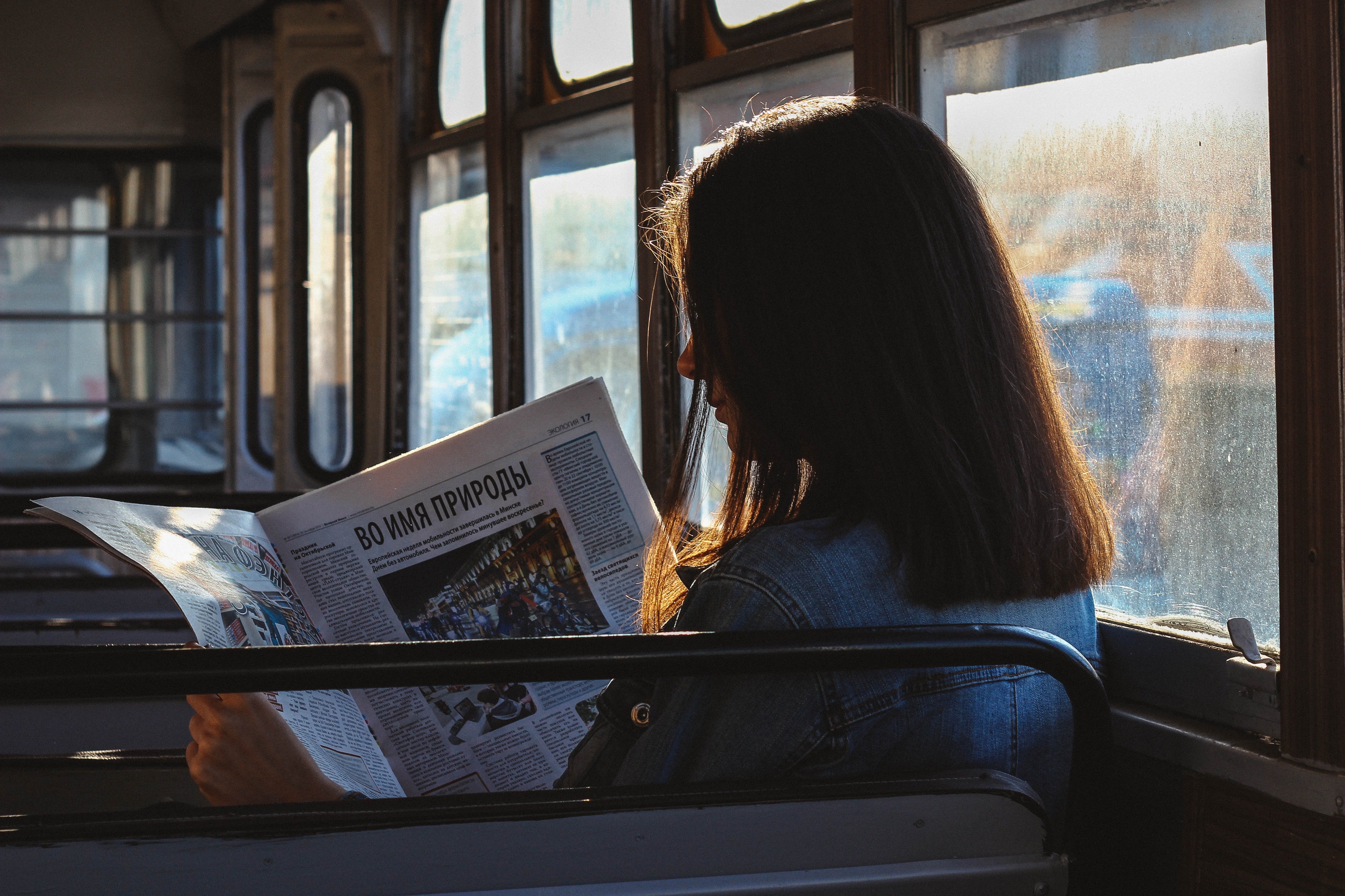 A woman reading a newspaper inside a bus | Photo: Pexels