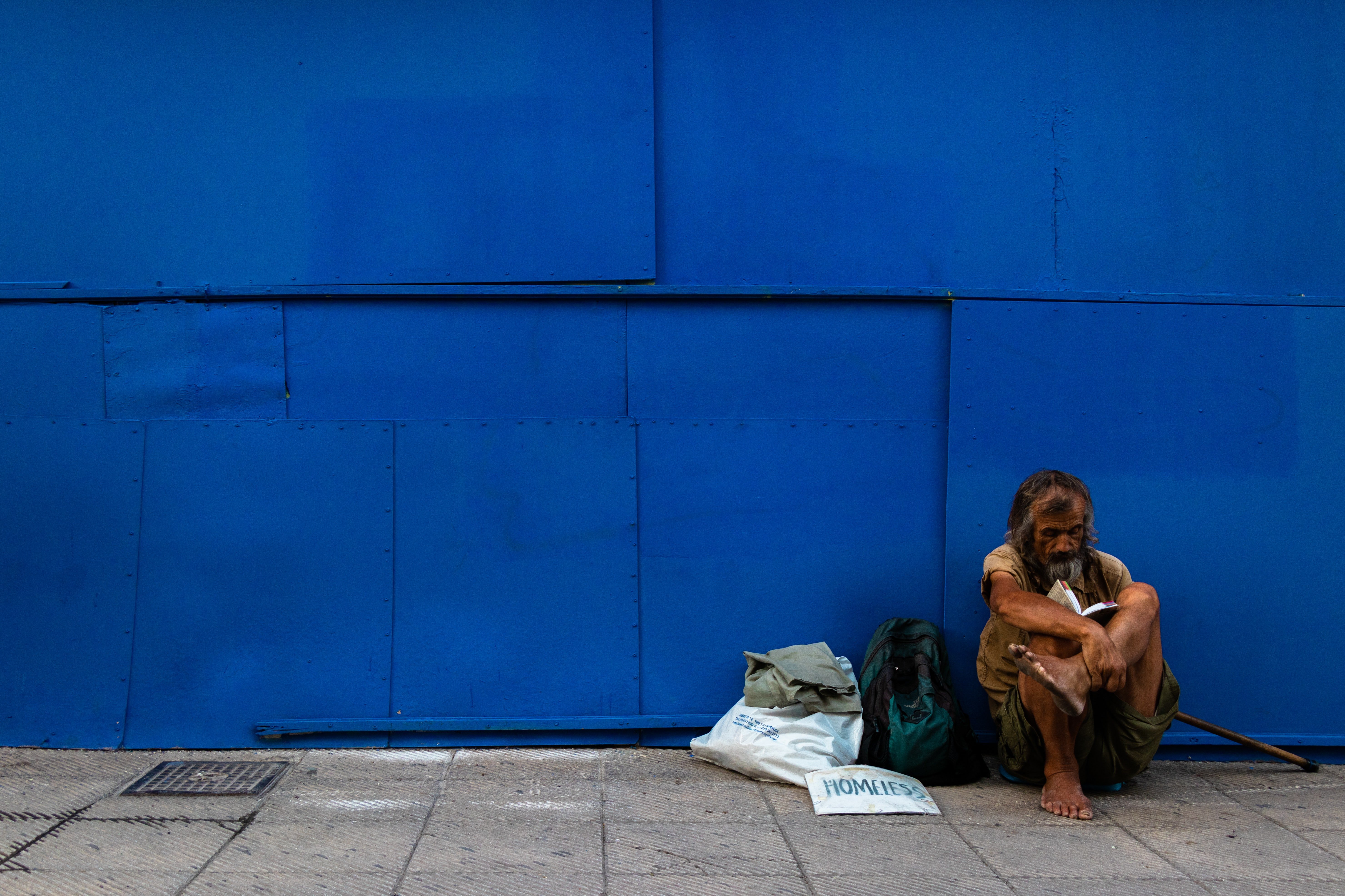 Man sitting against a blue wall sitting next to a couple of bags | Source: Unsplash / Jonathan Kho