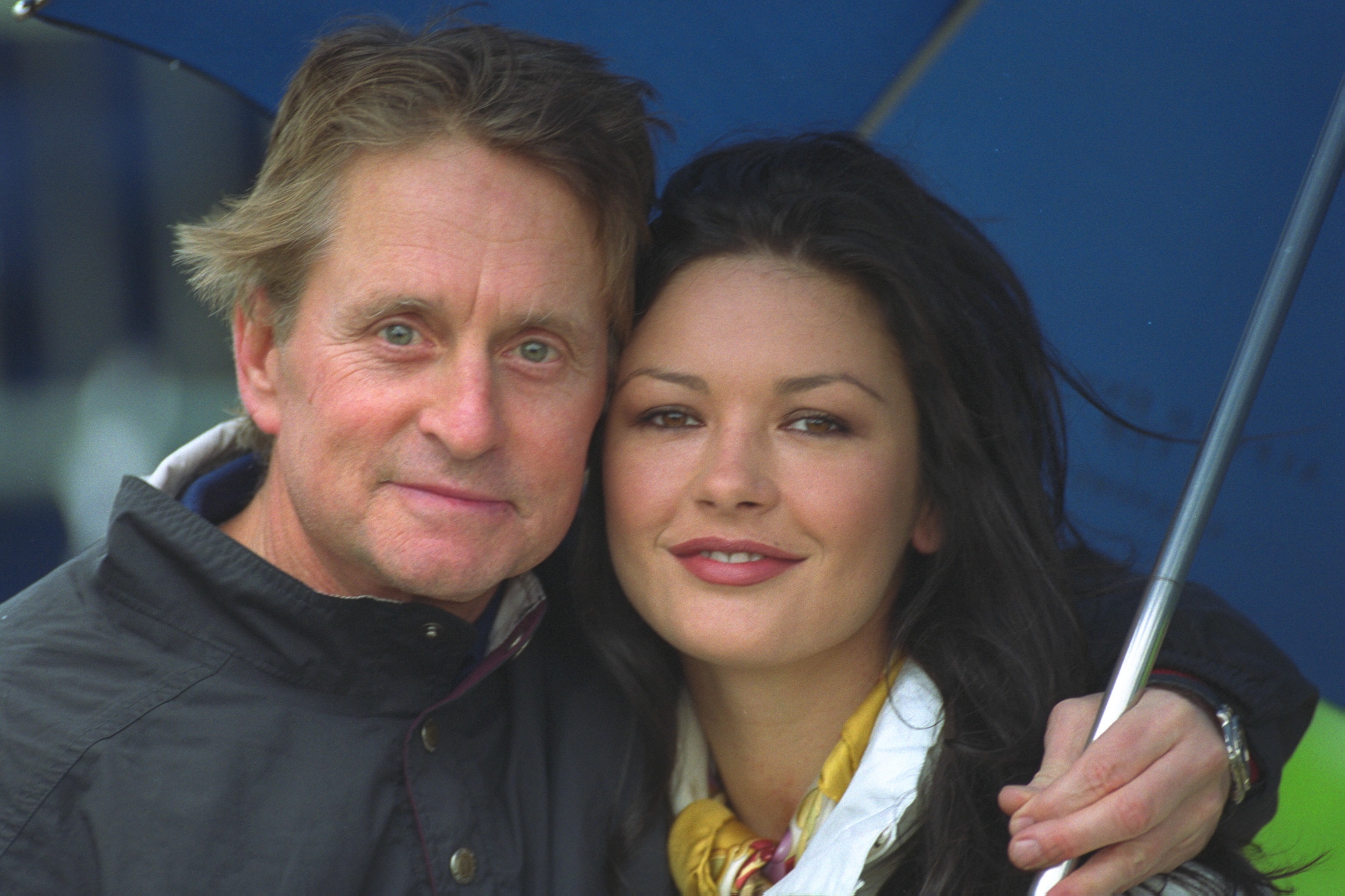 Michael Douglas and Catherine Zeta-Jones shelter from the drizzle while playing golf at St. Andrews. | Source: Getty Images