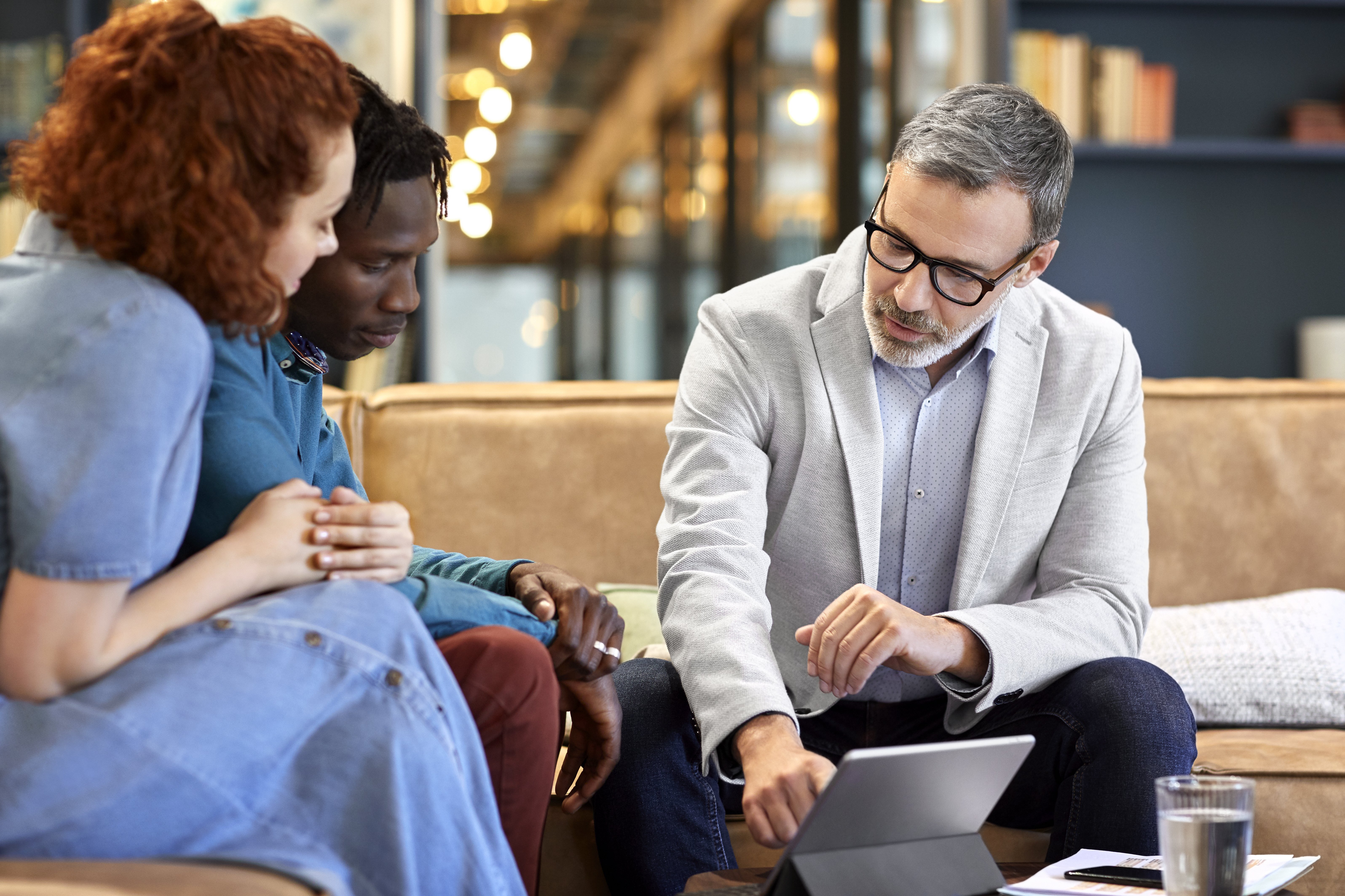 Mature financial advisor planning with young multi-ethnic couple at office. Businessman is discussing over digital tablet with clients at workplace. They are sitting in meeting.|Photo: Getty Images