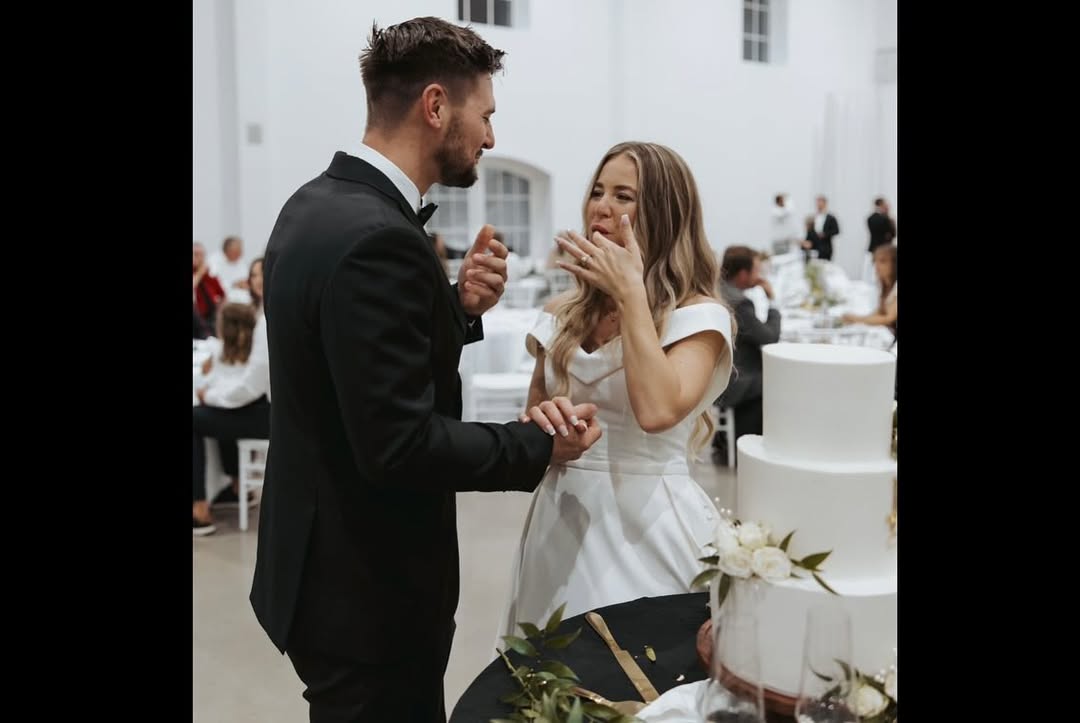 Jana Duggar shares a lighthearted moment with Stephen Wissmann as they feed each other cake, standing hand in hand beside their elegant white wedding cake. | Source: Instagram/janamduggar