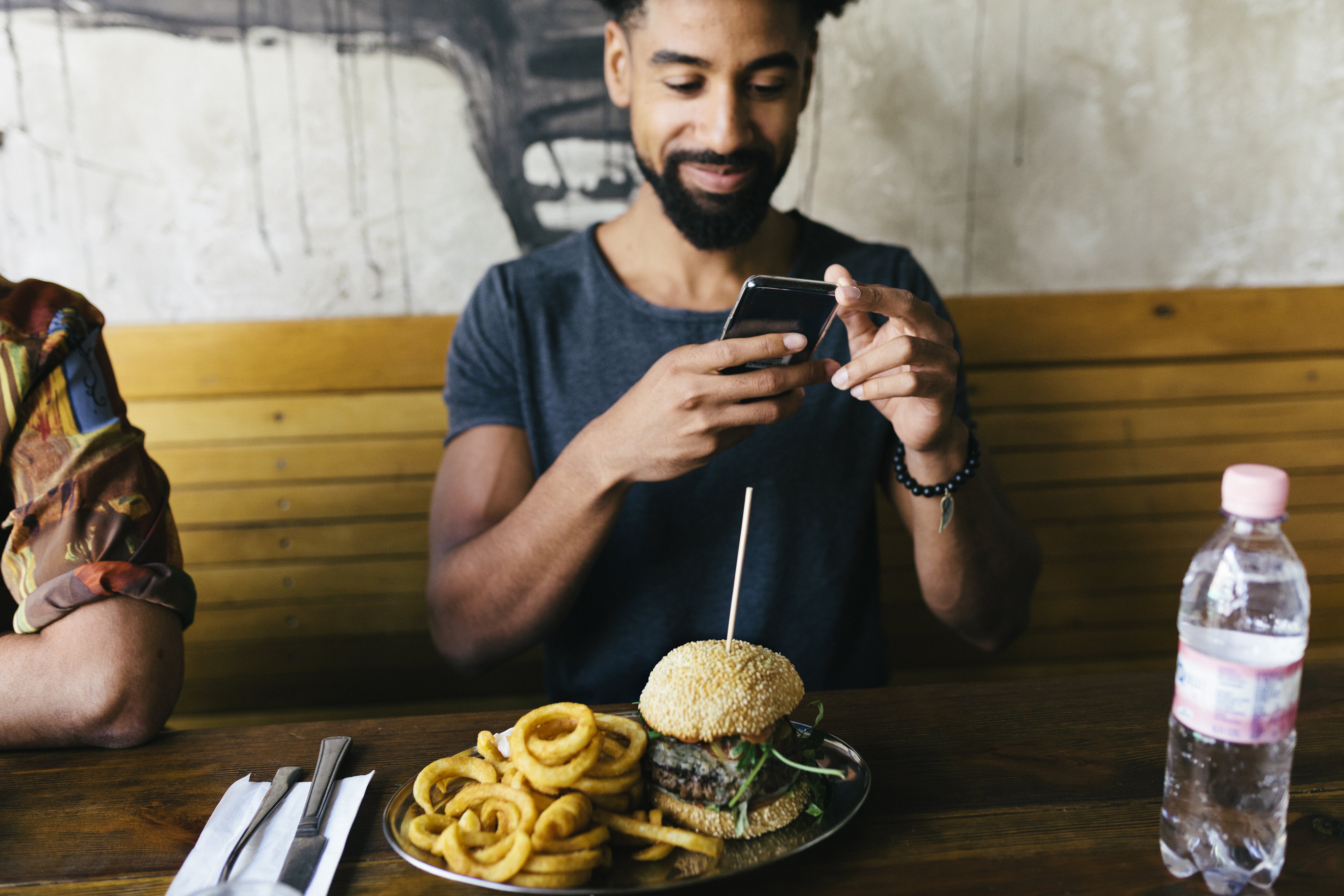 A man using his smartphone, taking photos of his burger before eating it at a trendy restaurant. | Photo: Getty Images