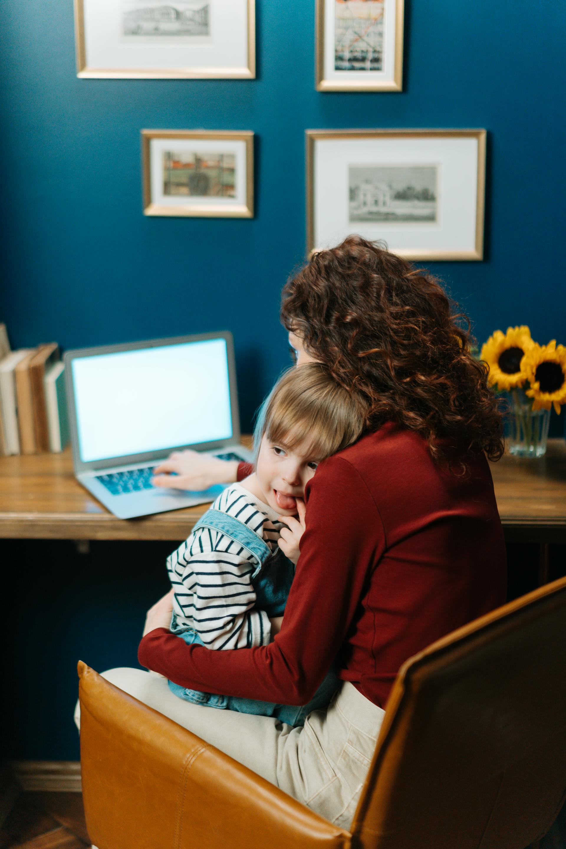 A woman holding a little boy while working on the laptop | Source: Pexels