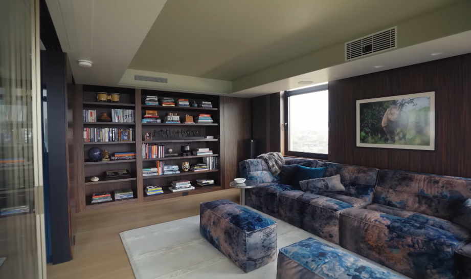 The media room trades the main living area's bright jewel tones for something far moodier and more enveloping. Books, dark timber and richly patterned upholstery make it one of the coziest corners of the home. | Source: YouTube/Architectural Digest