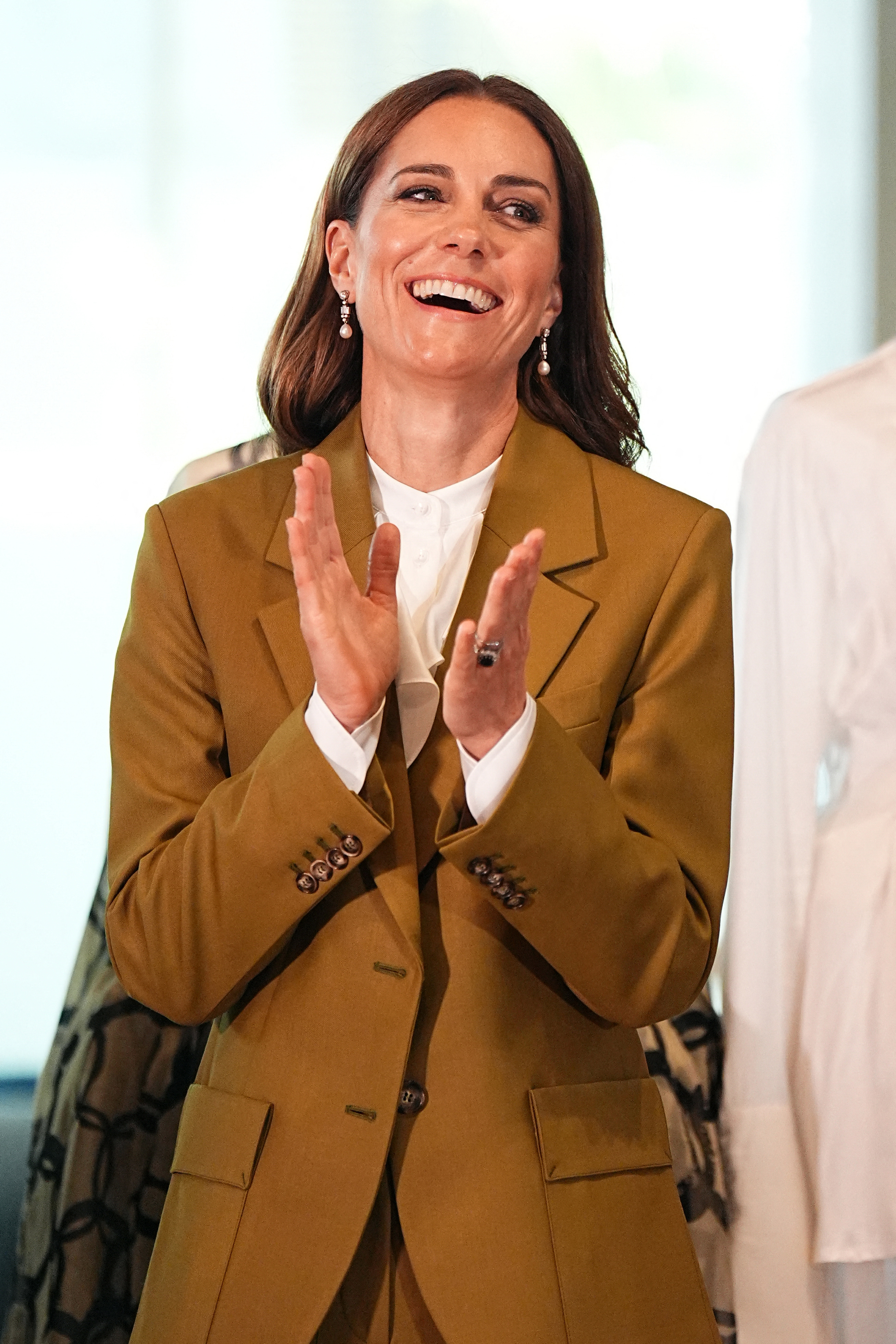Catherine is deeply immersed in the moment, throwing her head back in laughter as she claps with joy, fully celebrating the occasion, the artistry, and the vibrant creative talent surrounding her.