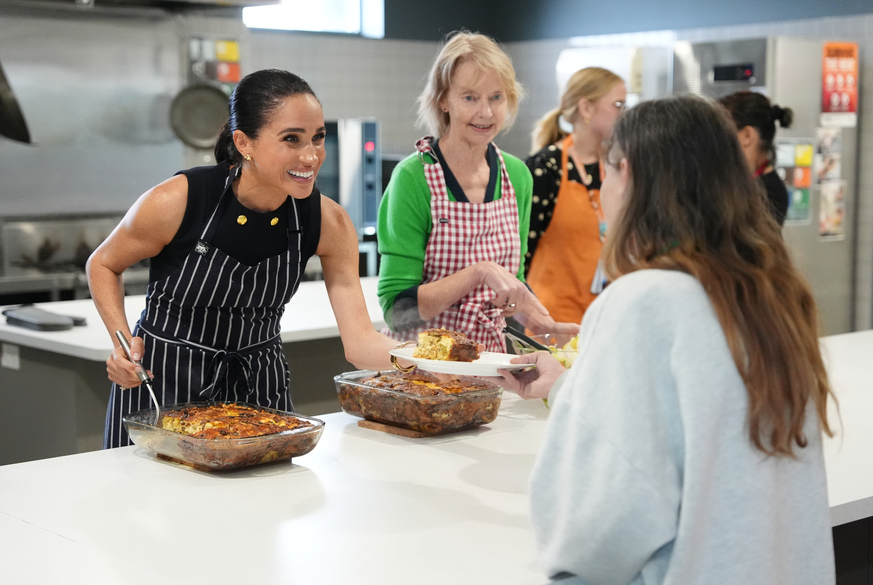 Meghan, Duchess of Sussex, and staff at McAuley Community Services for Women, a women's homeless and family violence shelter, serve lunch to a resident on 14 April 2026 in Melbourne, Australia. | Source: Getty Images