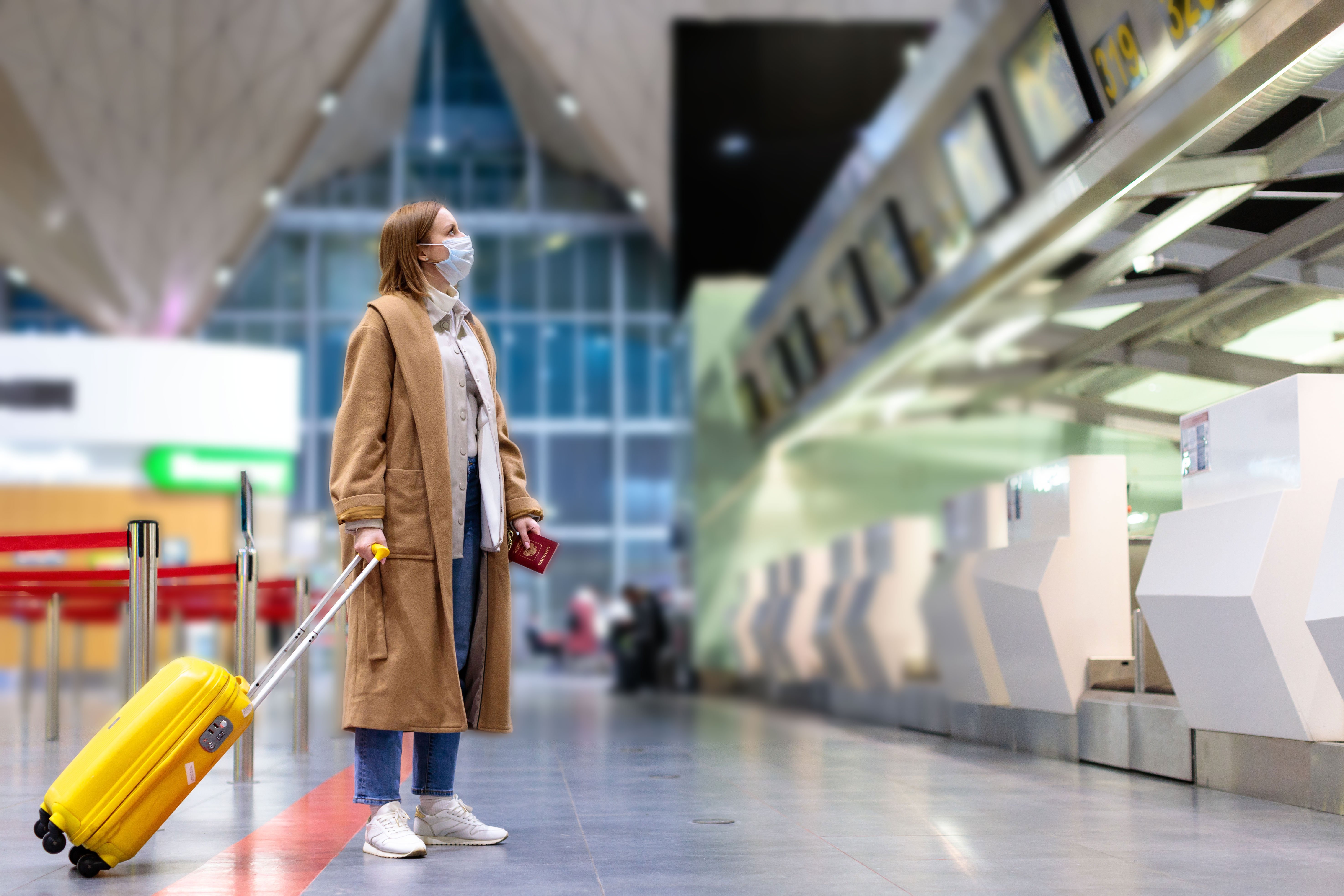 Woman with luggage standing at in front of a check-in counter at the airport terminal during the Covid-19 pandemic | Photo: Shutterstock