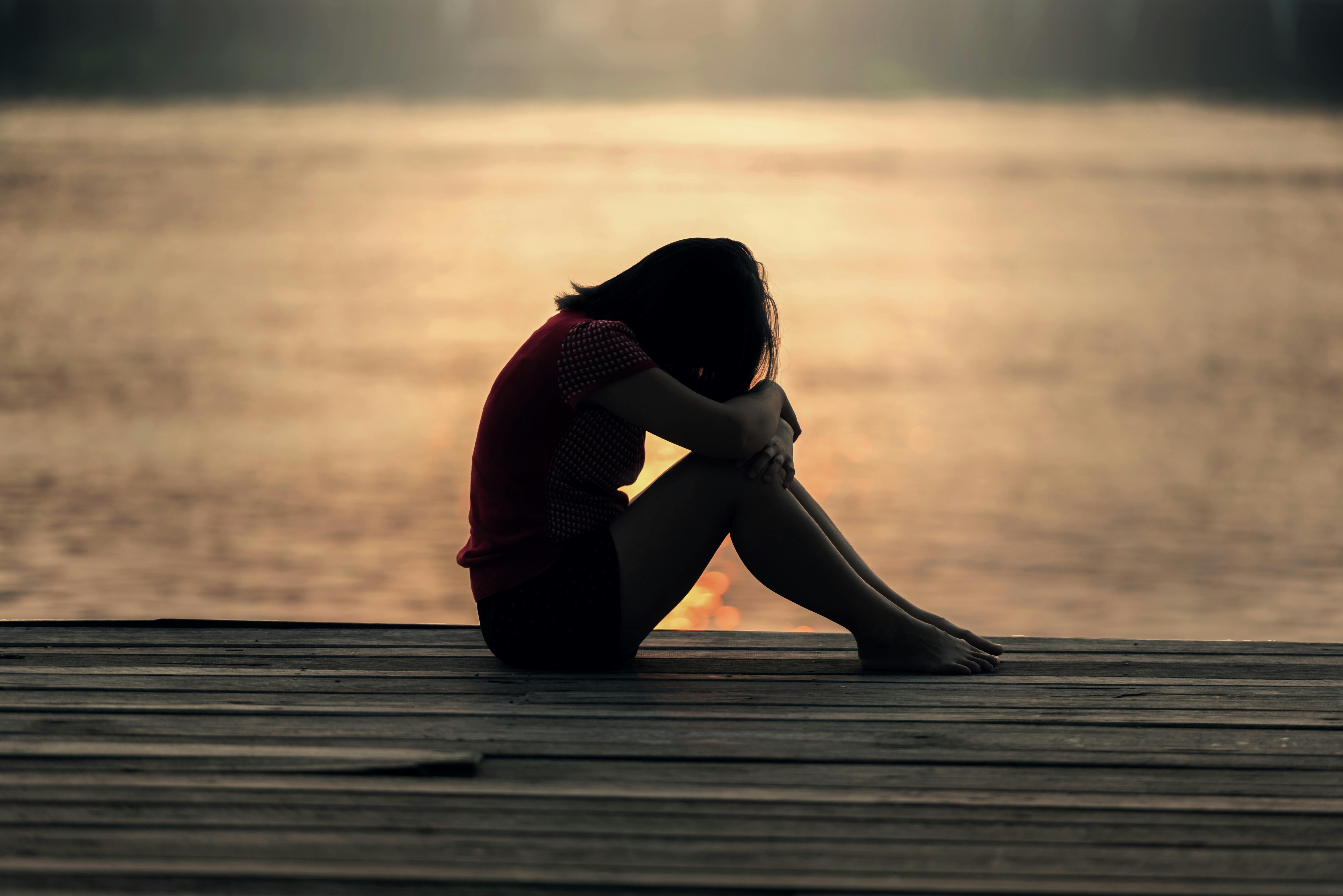 A silhouette of a  woman sitting, with her head on her knees, against the backdrop of the sunset | Source: Pexels