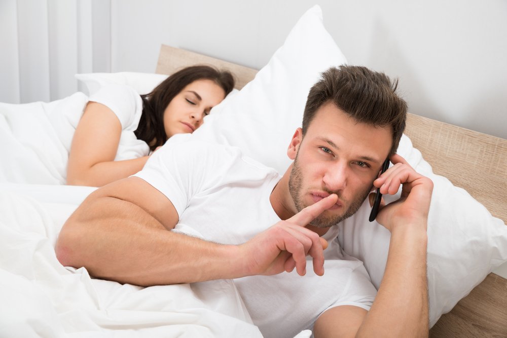 Hombre hablando por teléfono mientras su esposa duerme. | Foto: Shutterstock
