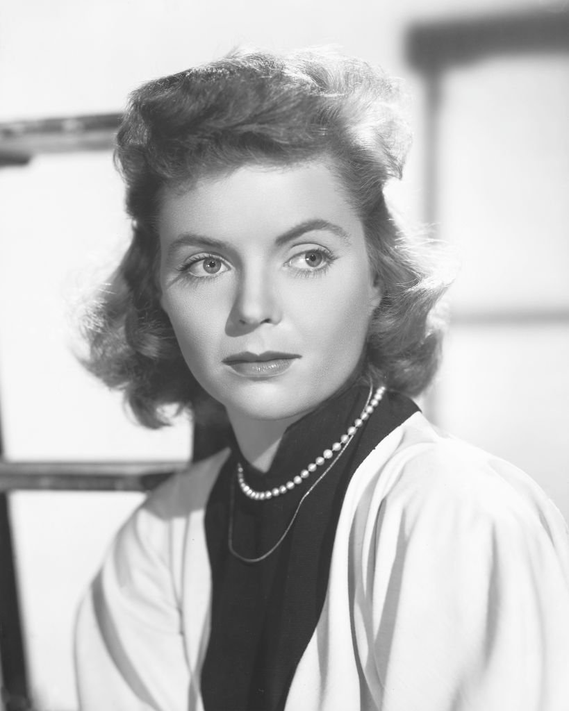 Dorothy McGuire (1916-2001) wearing a white cardigan over a black high-neck blouse with a pearl necklace, in a studio portrait, circa 1950. | Photo: Getty Images