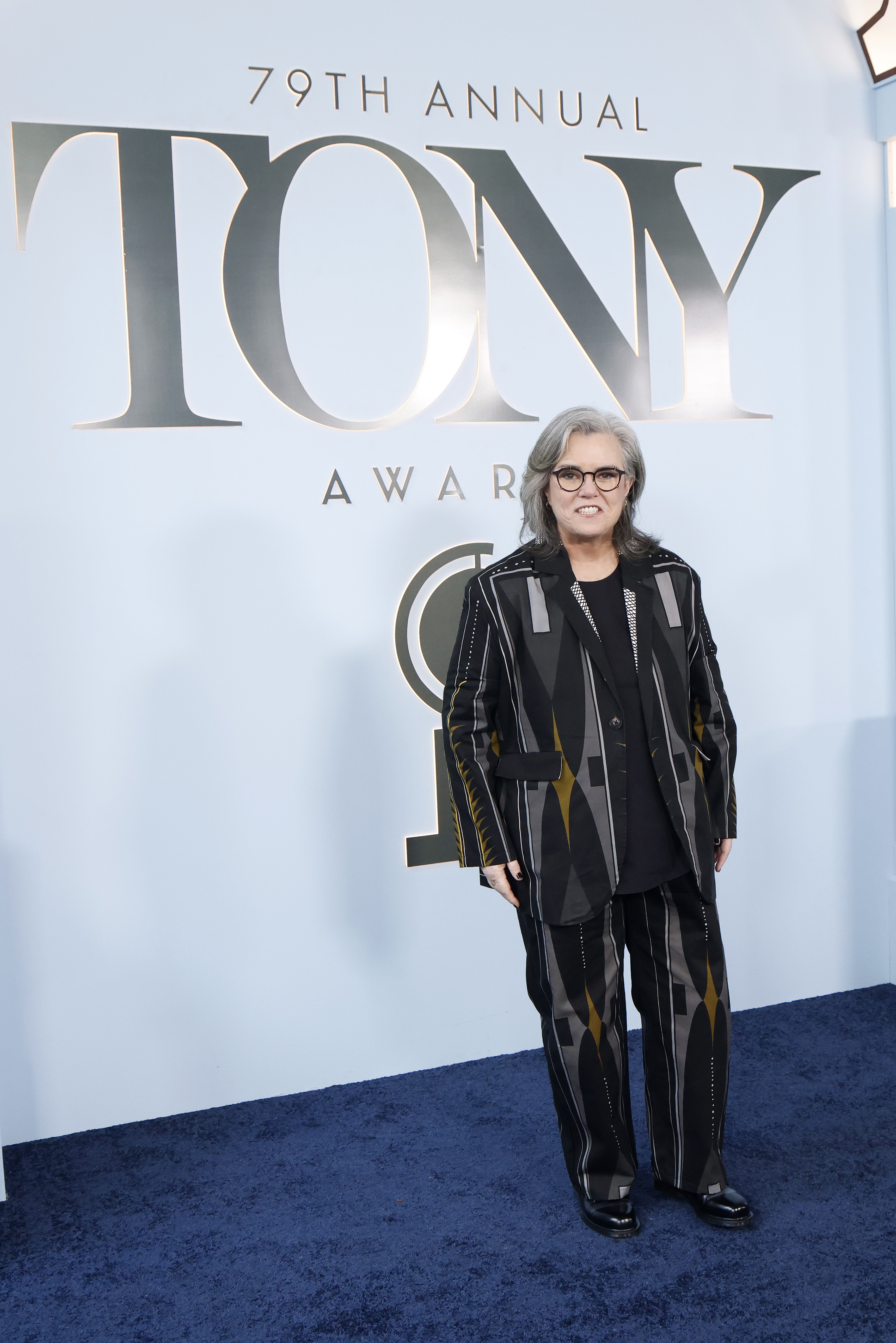 Rosie O'Donnell poses beneath the oversized Tony Awards logo as she arrives at Radio City Music Hall in a black patterned suit. At this point, the attention was still on Broadway's biggest night rather than her appearance.