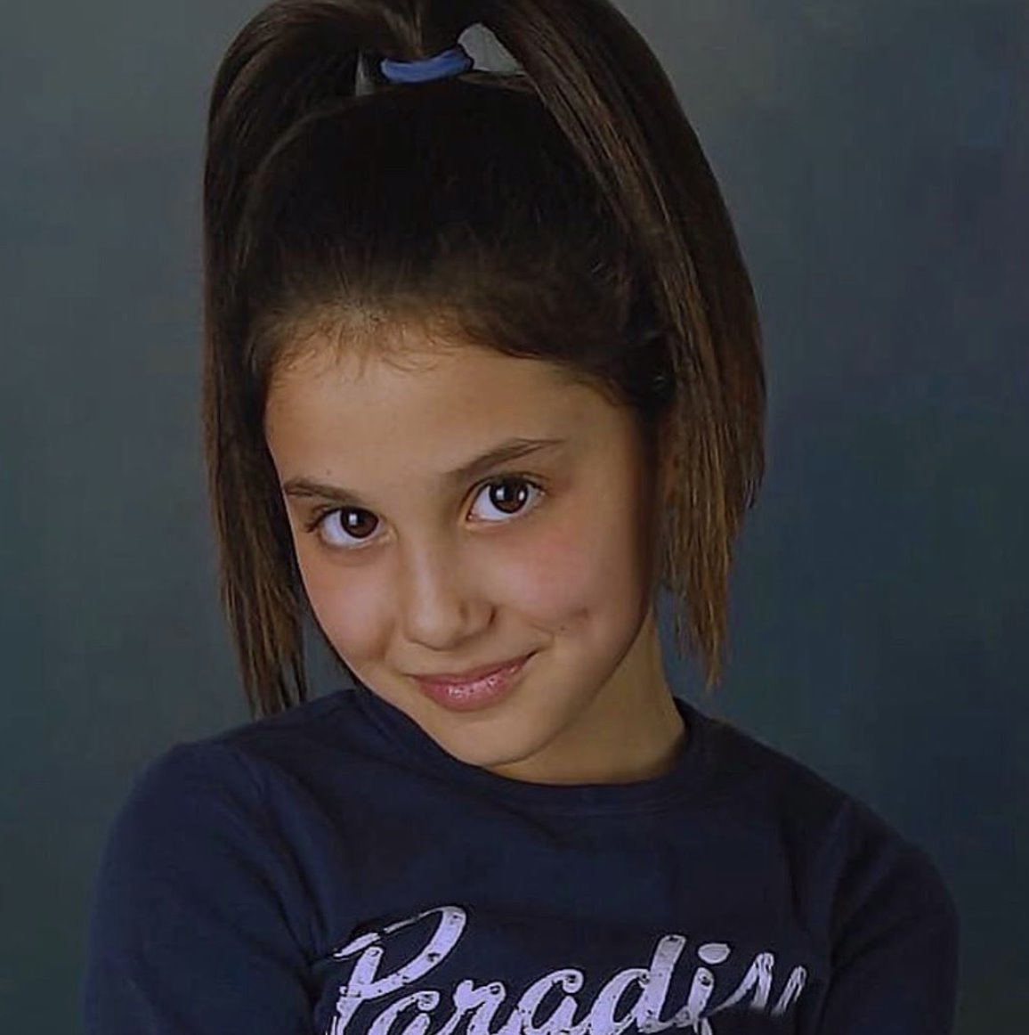 A school-age Ariana Grande with a high ponytail and playful grin, already posing with the quiet confidence of a star in the making | Source: Facebook/GraziaUK