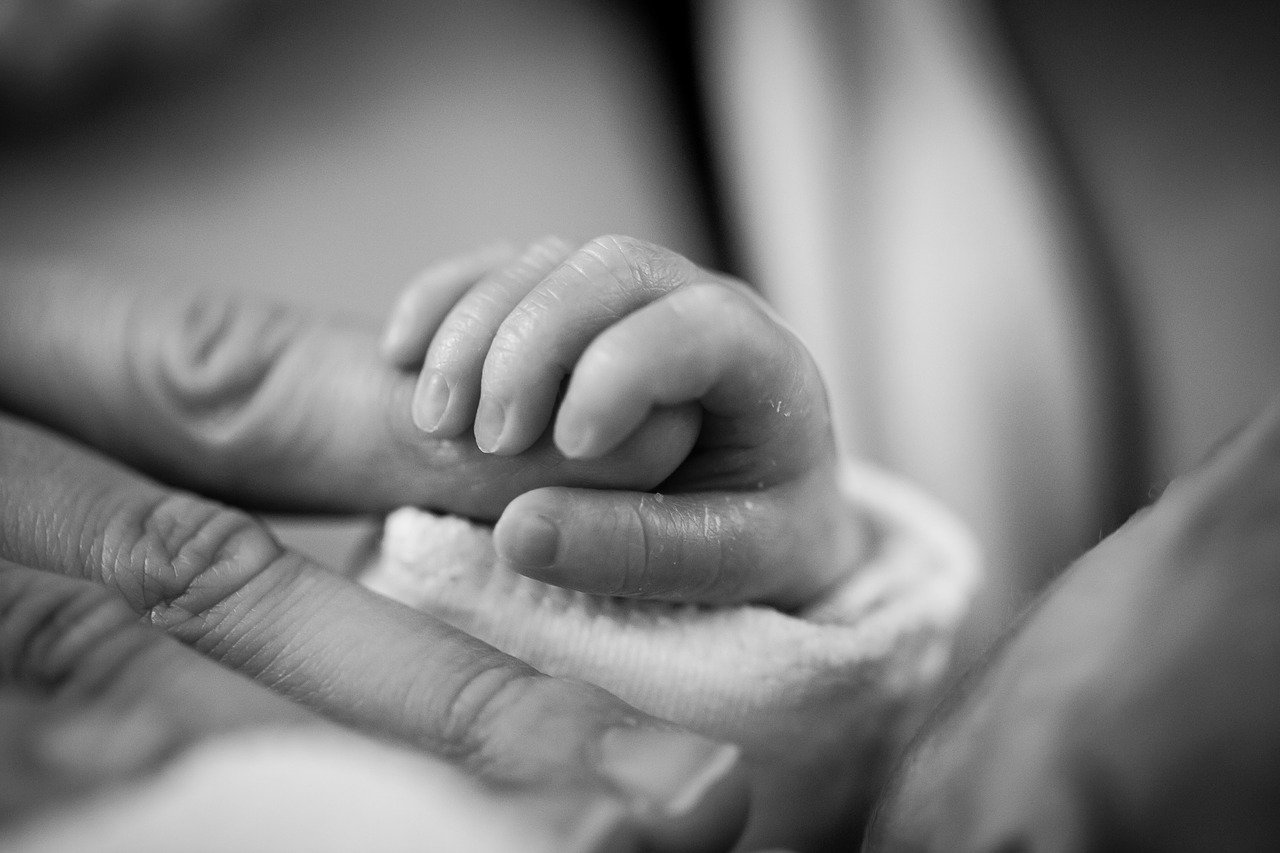 A newborn baby holds and adult's finger in this black-and-white image | Photo: Pixabay/SeppH