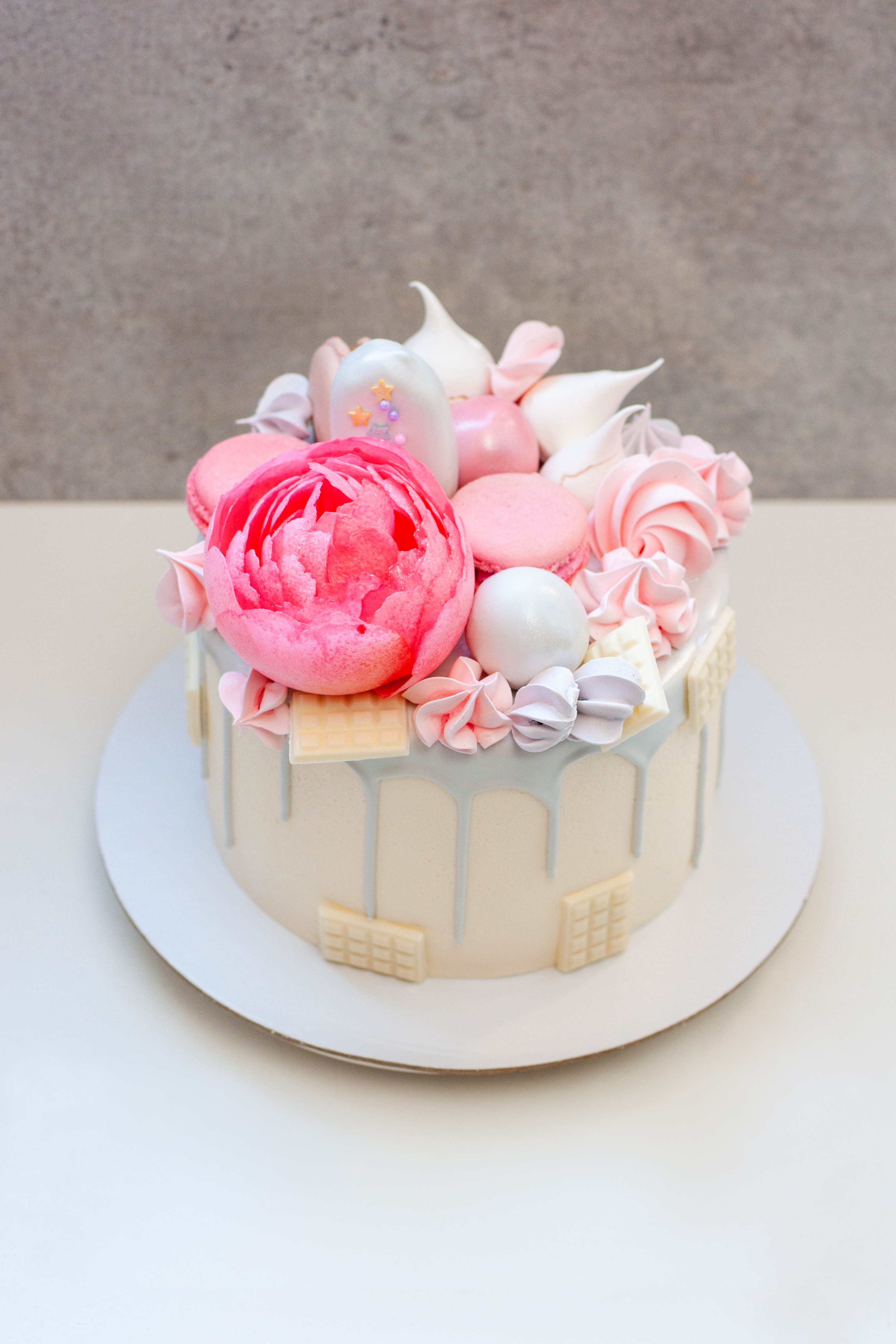 Beautiful and elegant cake decorated with melted grey chocolate, macaroons, edible pink peony flower, chocolate bites and meringues | Source: Getty Images