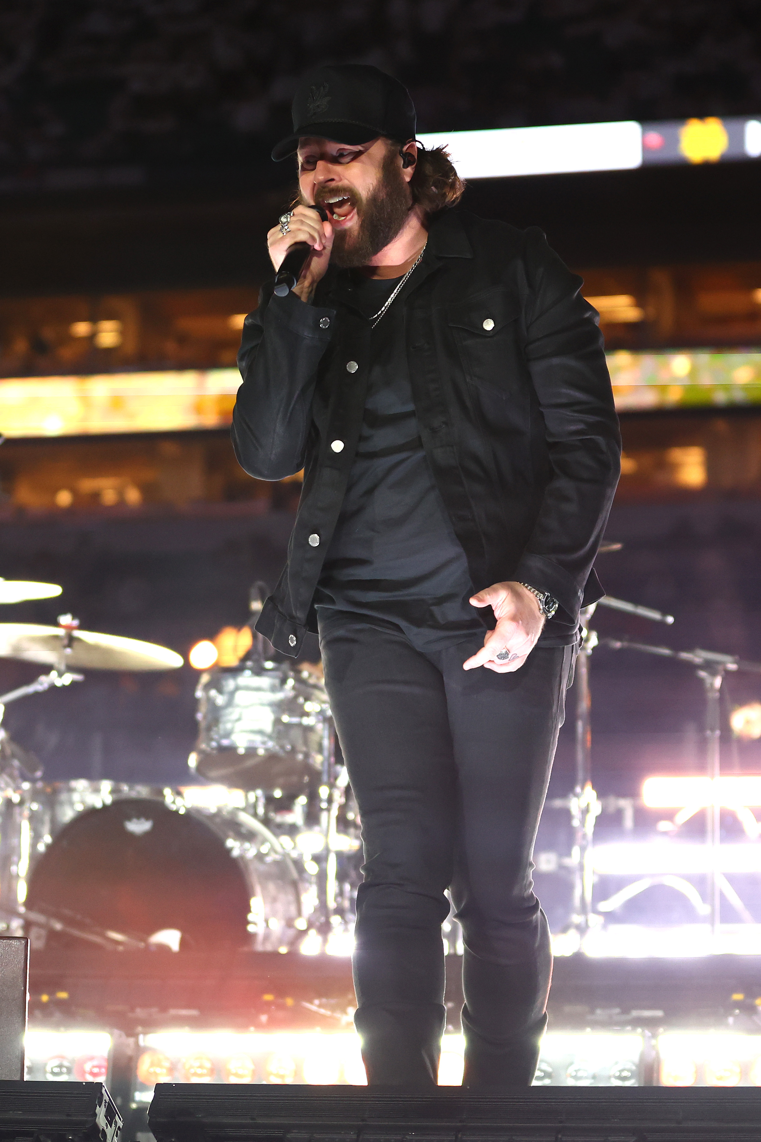 Nate Smith sings into a handheld microphone in an all-black ensemble, delivering a powerful halftime performance with the stadium lights blazing behind him.