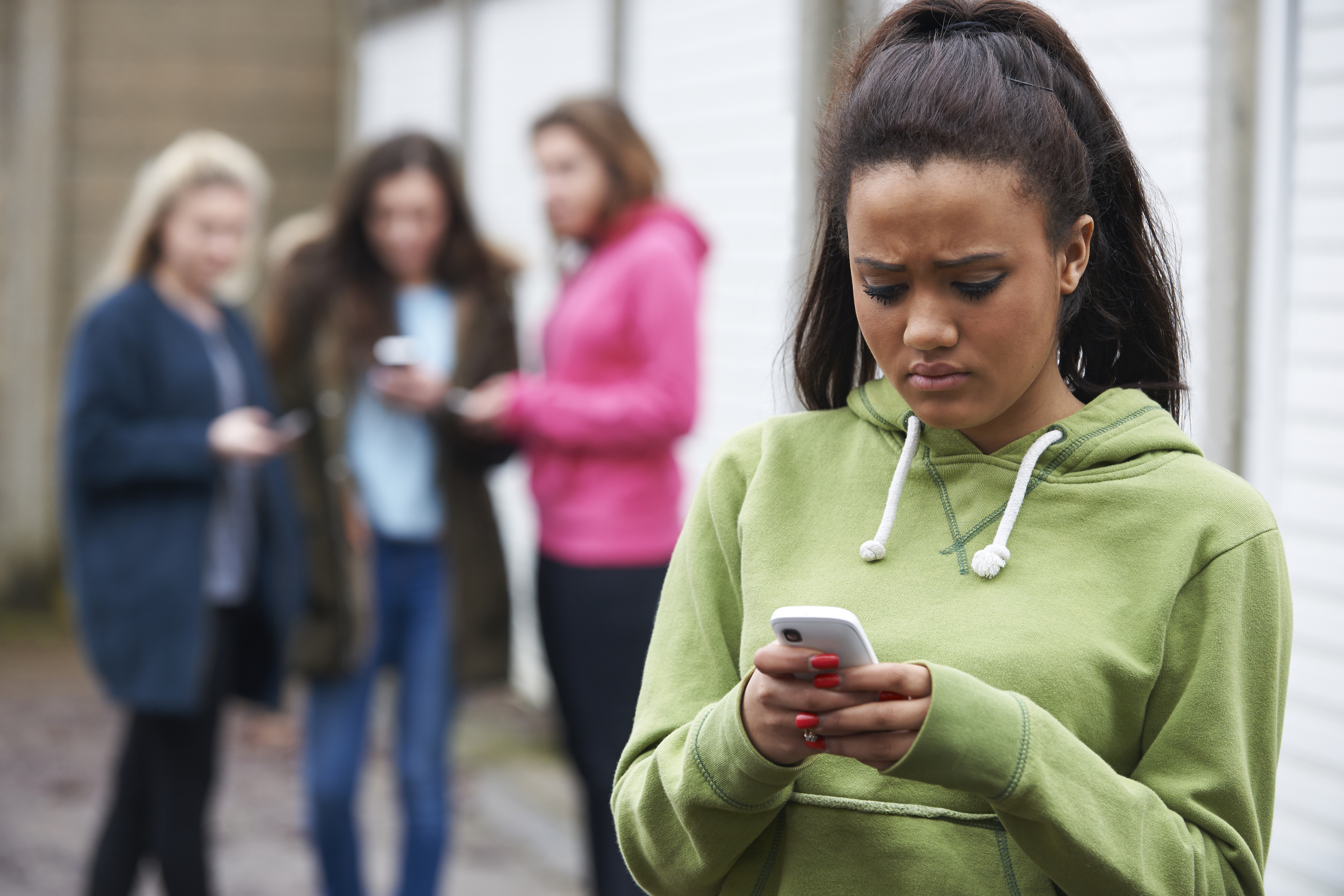 Girl looking worried while looking as she looks at her phone while other girls watching her behind | Source: Shutterstock