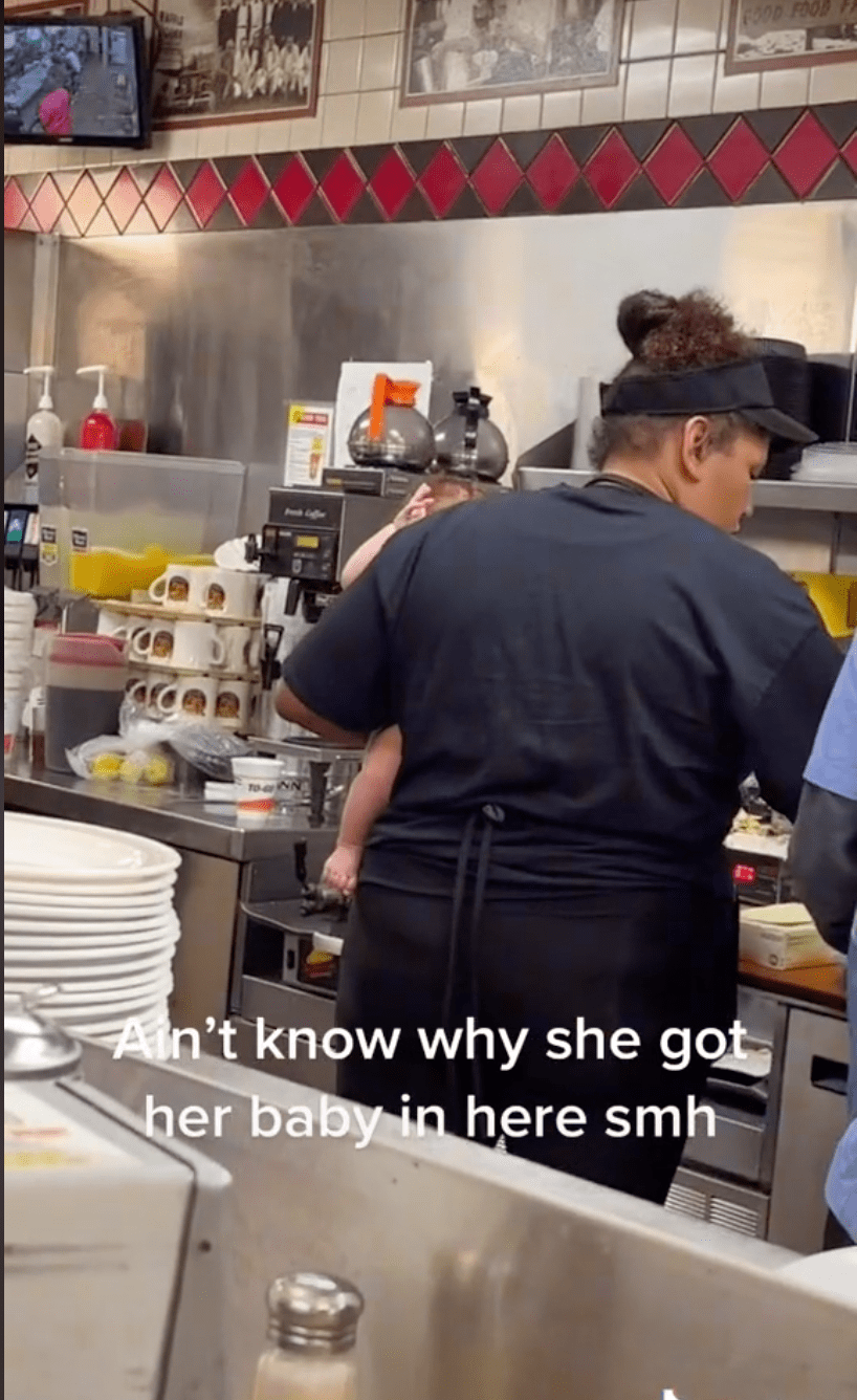 A Waffle House worker carries a child while preparing food for customers. | Source: Tiktok.com/kizzle360