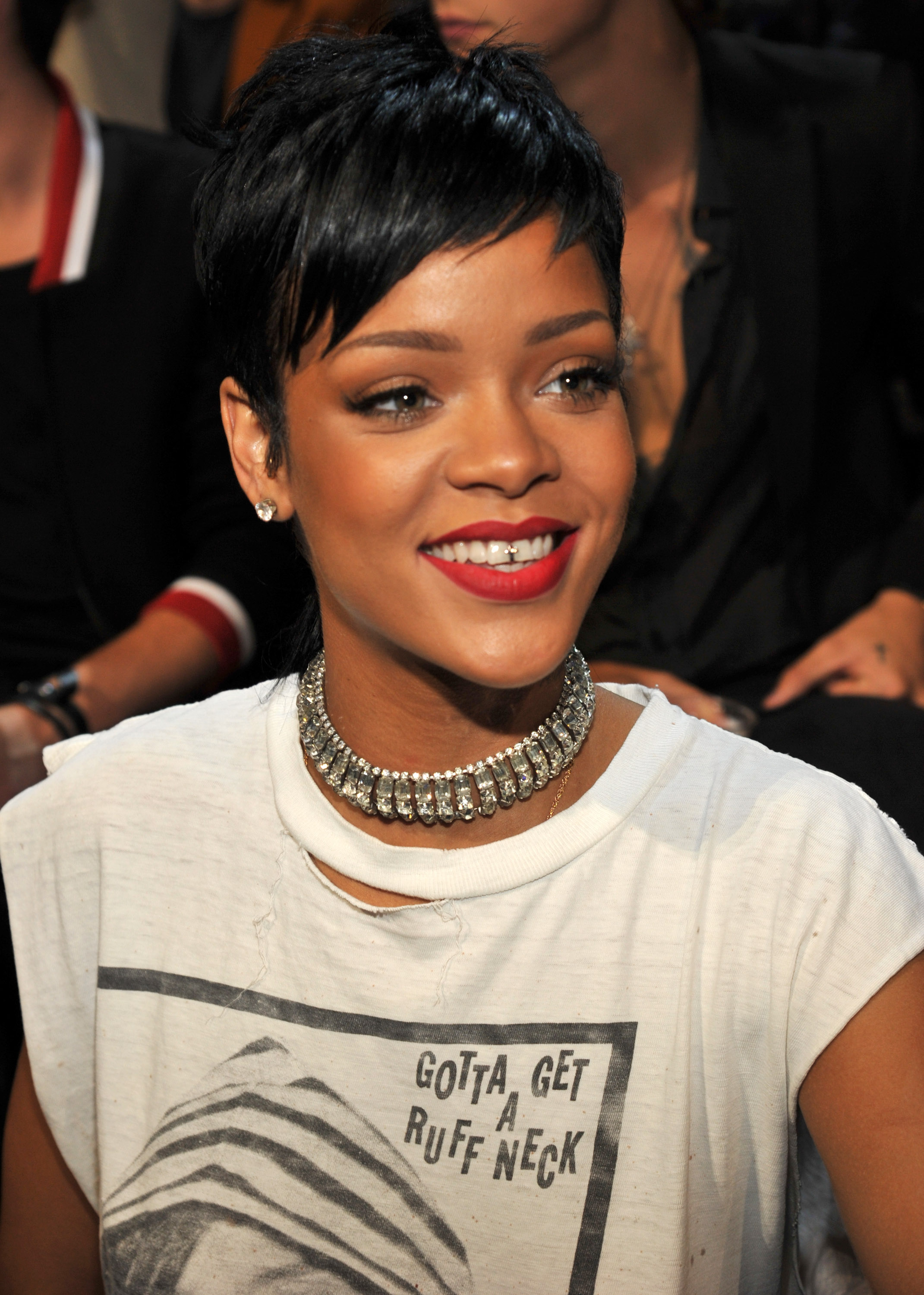 Rihanna beams with effortless cool at the MTV Video Music Awards, pairing a bold graphic tee with a dazzling choker and a striking red lip. Her cropped hairstyle sharpens the look, giving her a modern edge as she radiates confidence with the laid-back vibe only she can pull off.