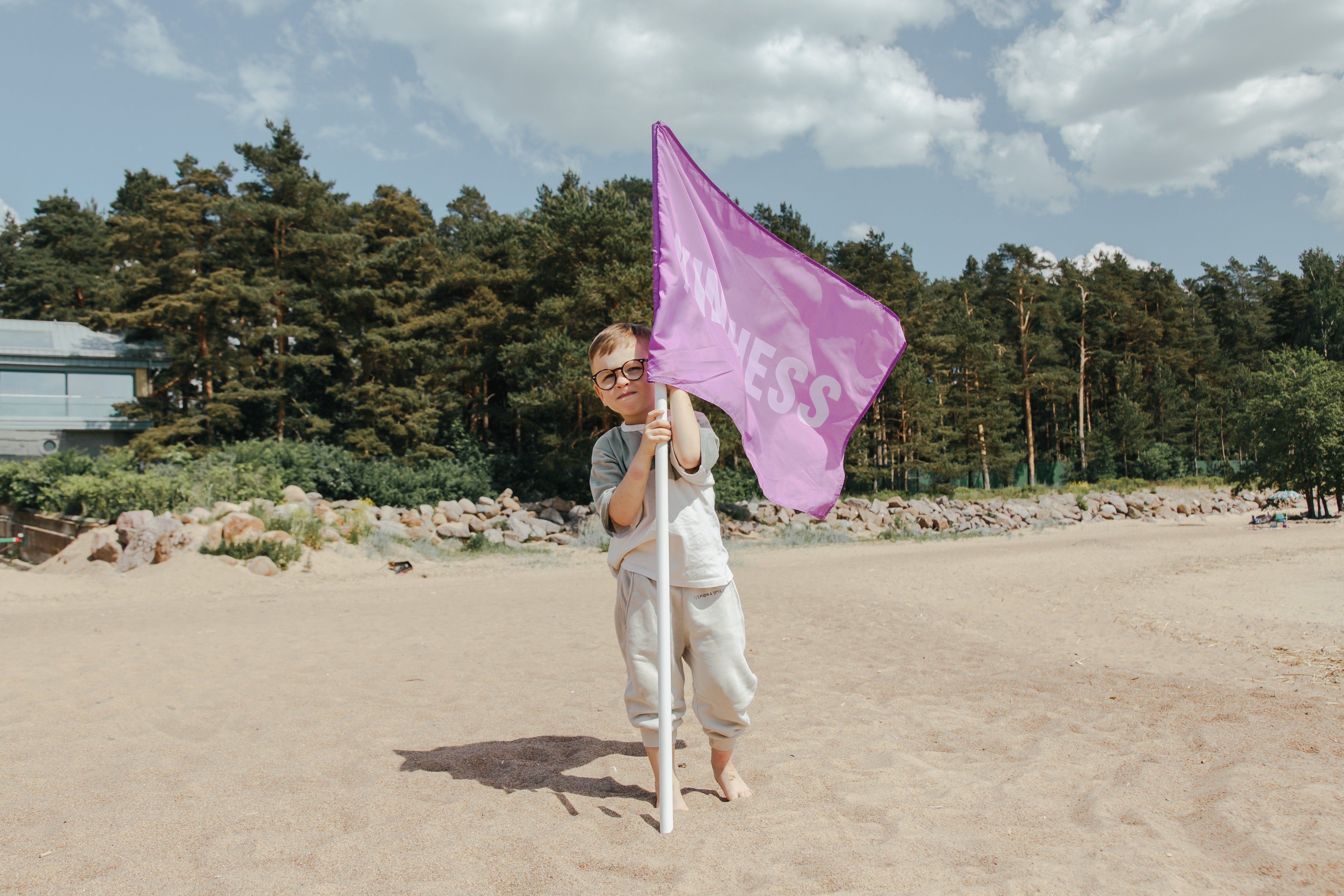 A boy holding a pink flag with the word 'Kindness' on it. | Photo: Pexels